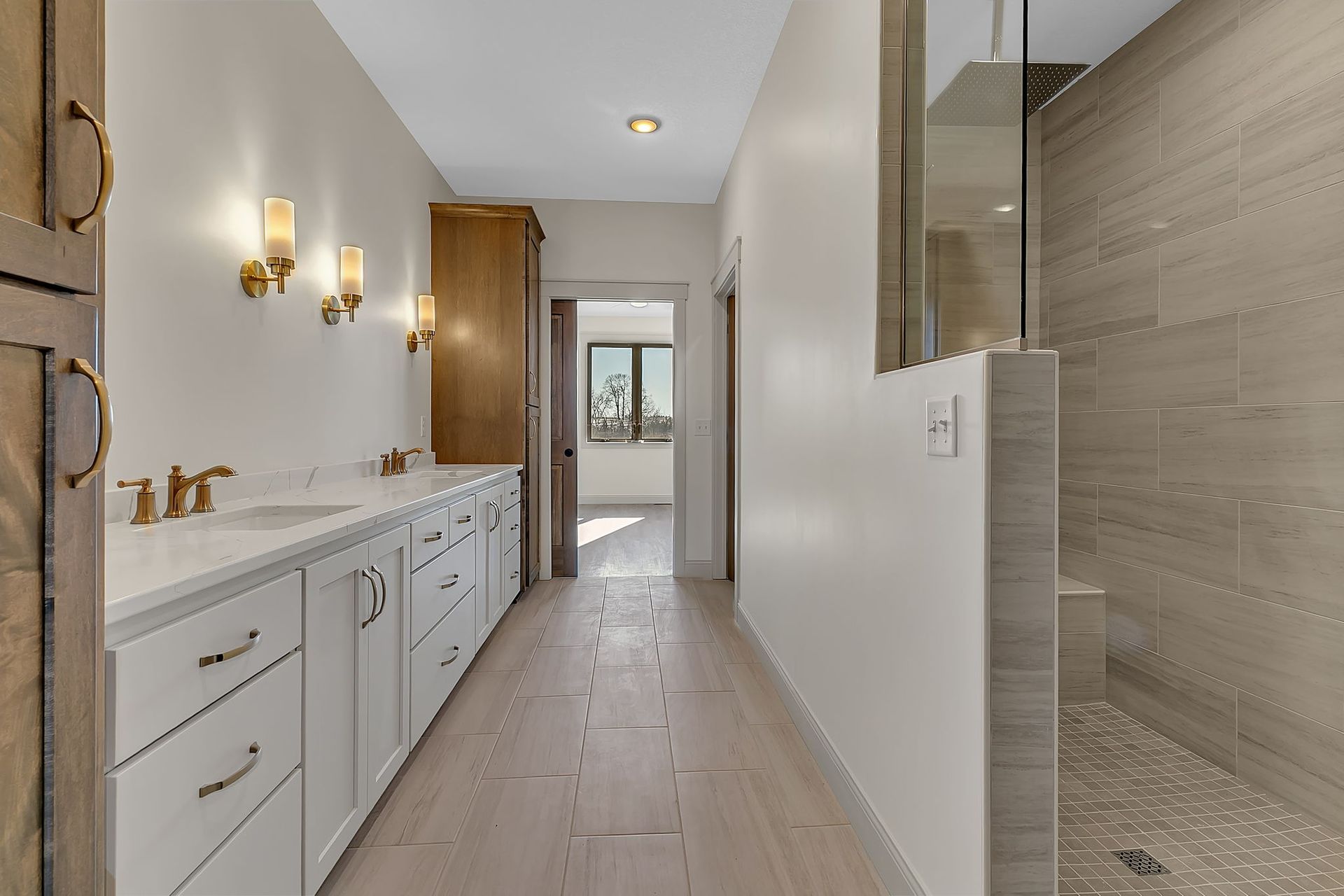 Bathroom with a long white vanity, gold fixtures, and a glass-walled shower.