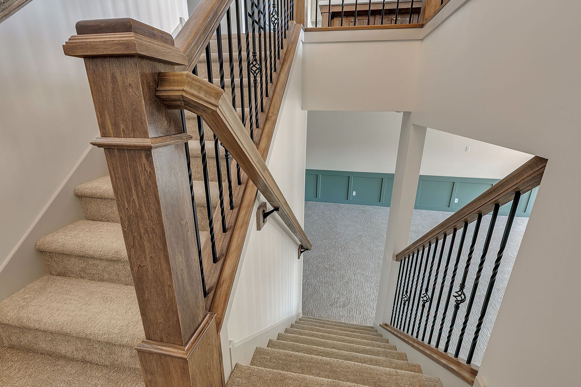 Staircase with carpeted steps, wooden handrails, and black iron balusters.