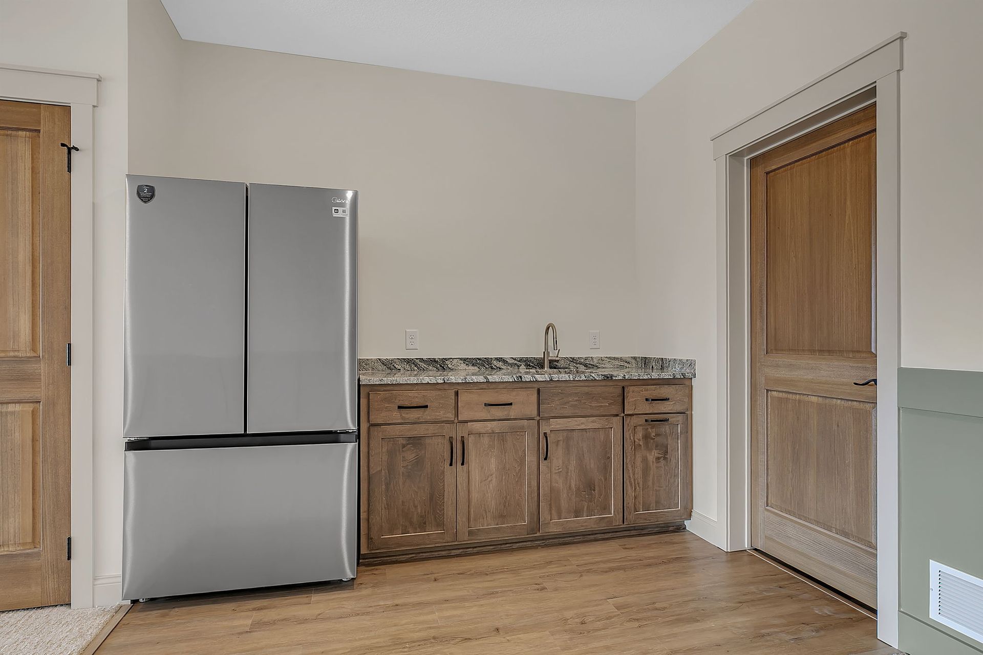 Kitchenette with a refrigerator, cabinets, and a sink. Two wooden doors are visible.