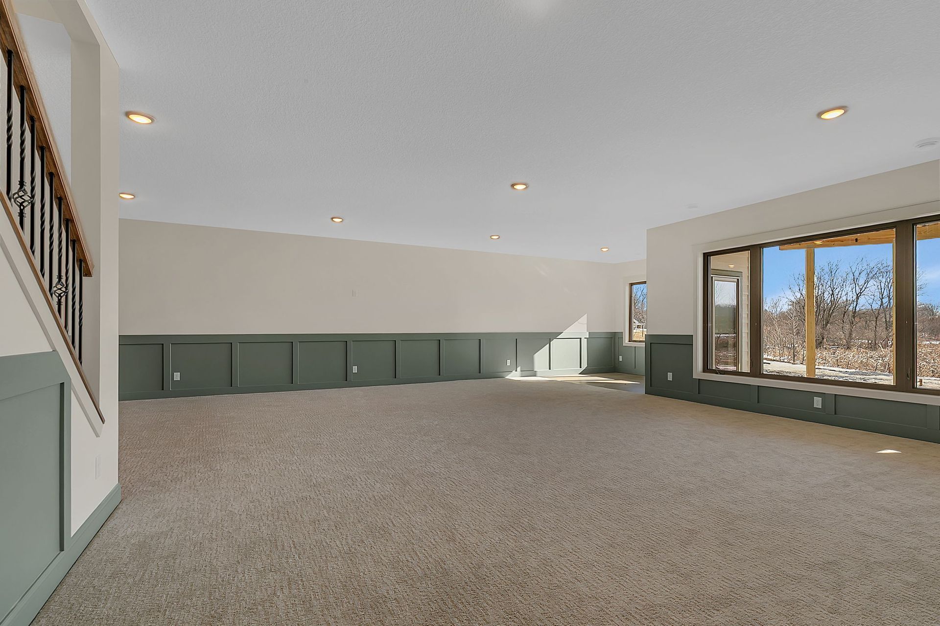 Empty room with beige carpet, green wainscoting, and large windows with outdoor view.