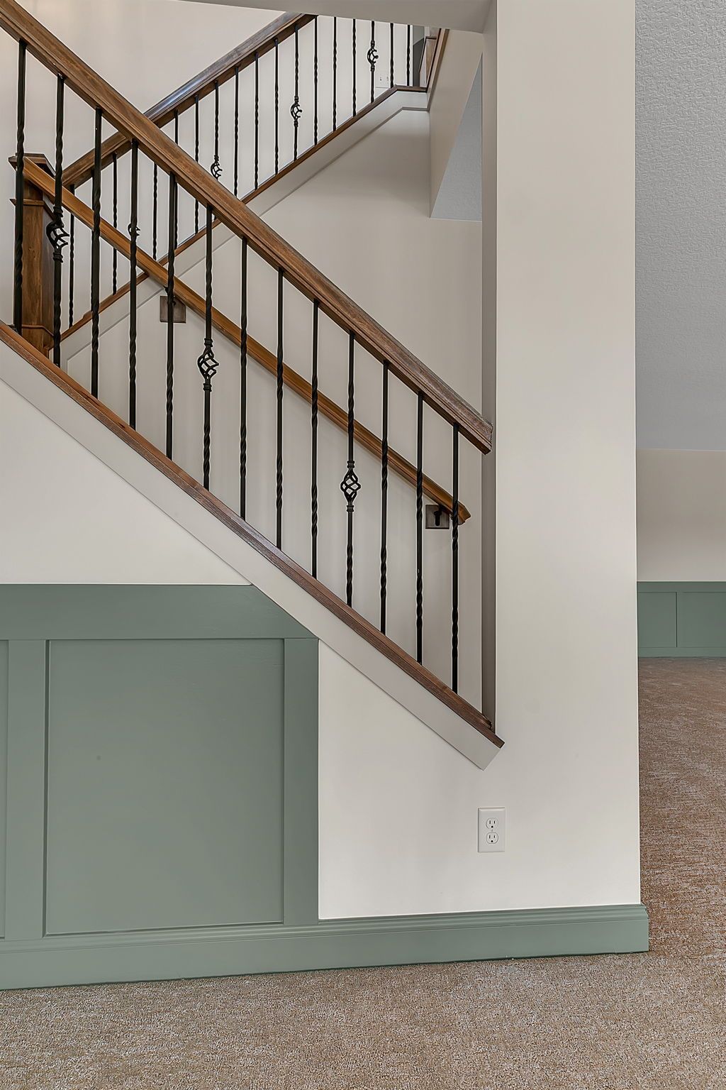 Staircase with wooden handrail and black iron spindles, built into a white wall. Green paneling.
