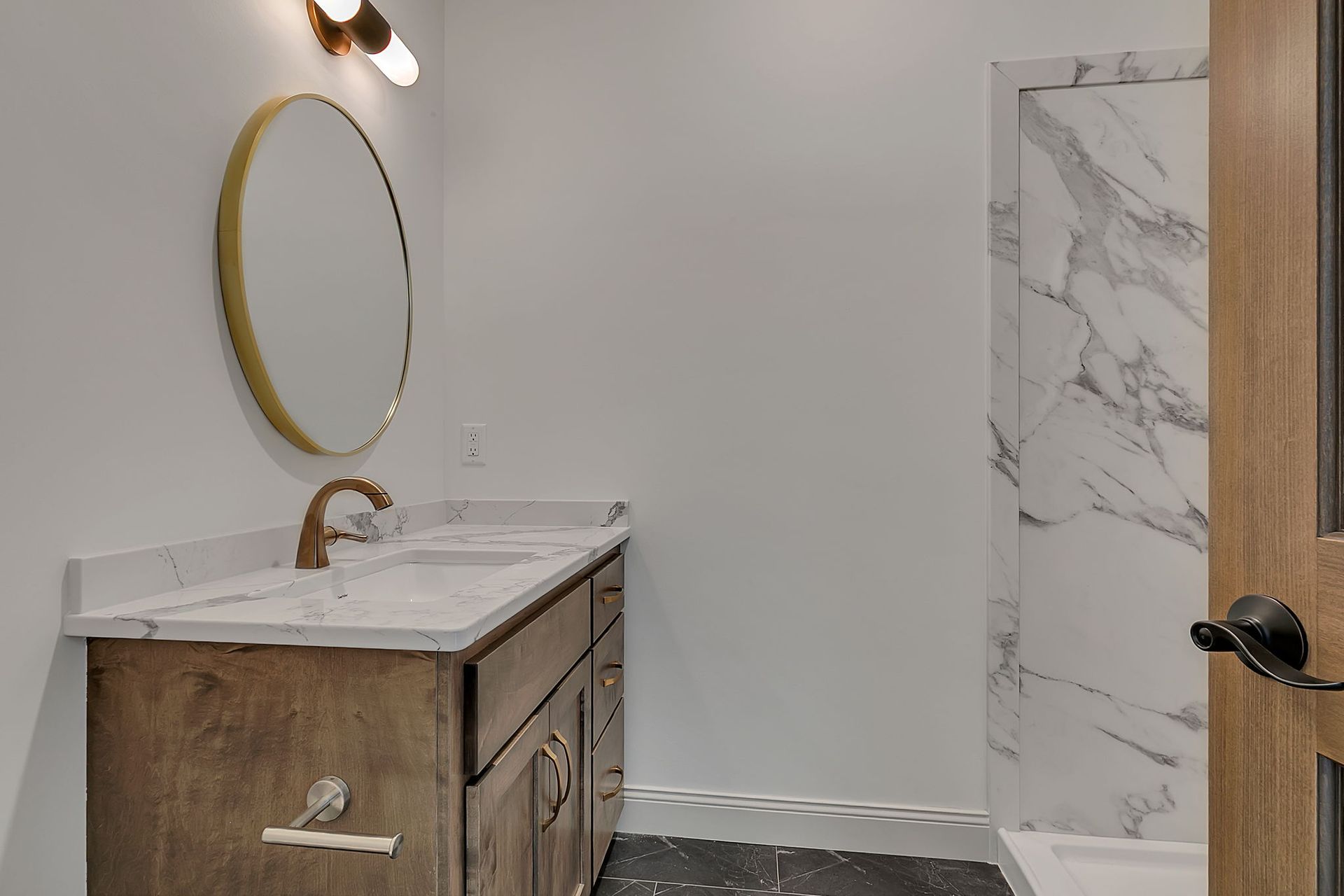 Bathroom with a brown vanity, gold mirror and faucet, and marble shower.