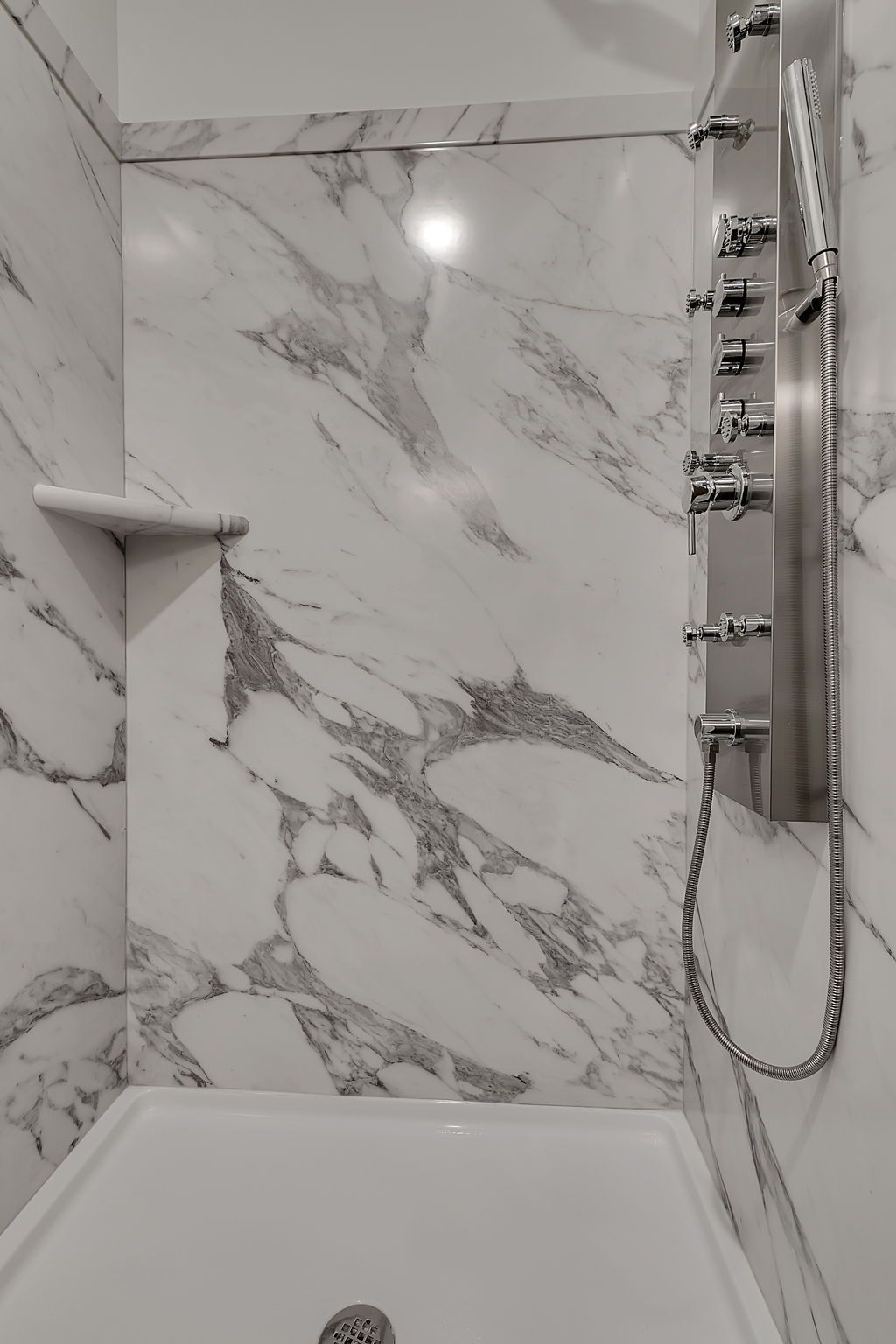 White marble shower with built-in shelf and multi-head shower fixture.