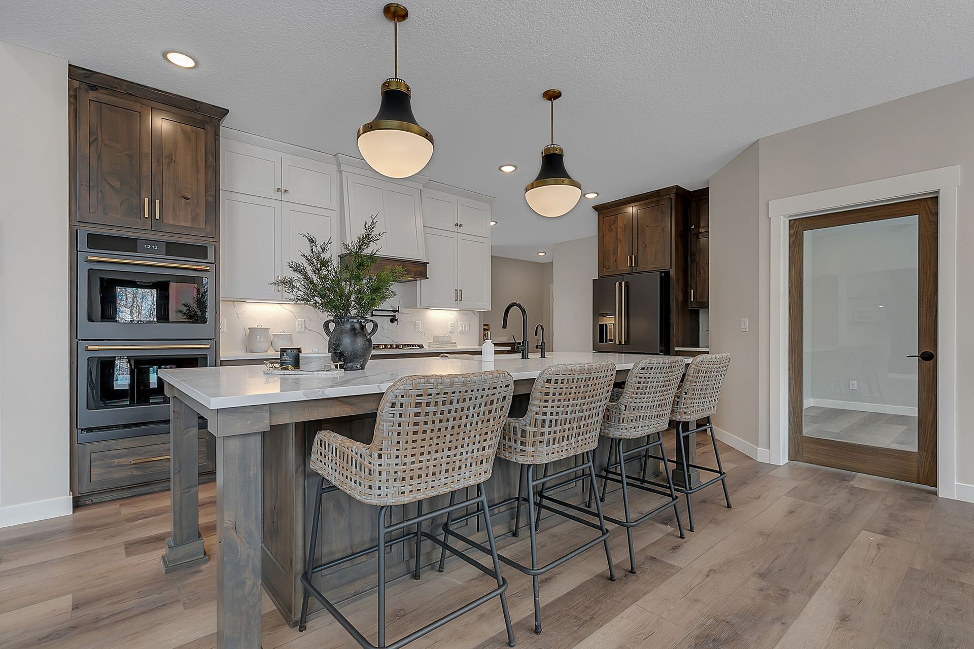 Modern kitchen with island, pendant lights, and bar stools. Wooden cabinets and flooring; neutral color palette.