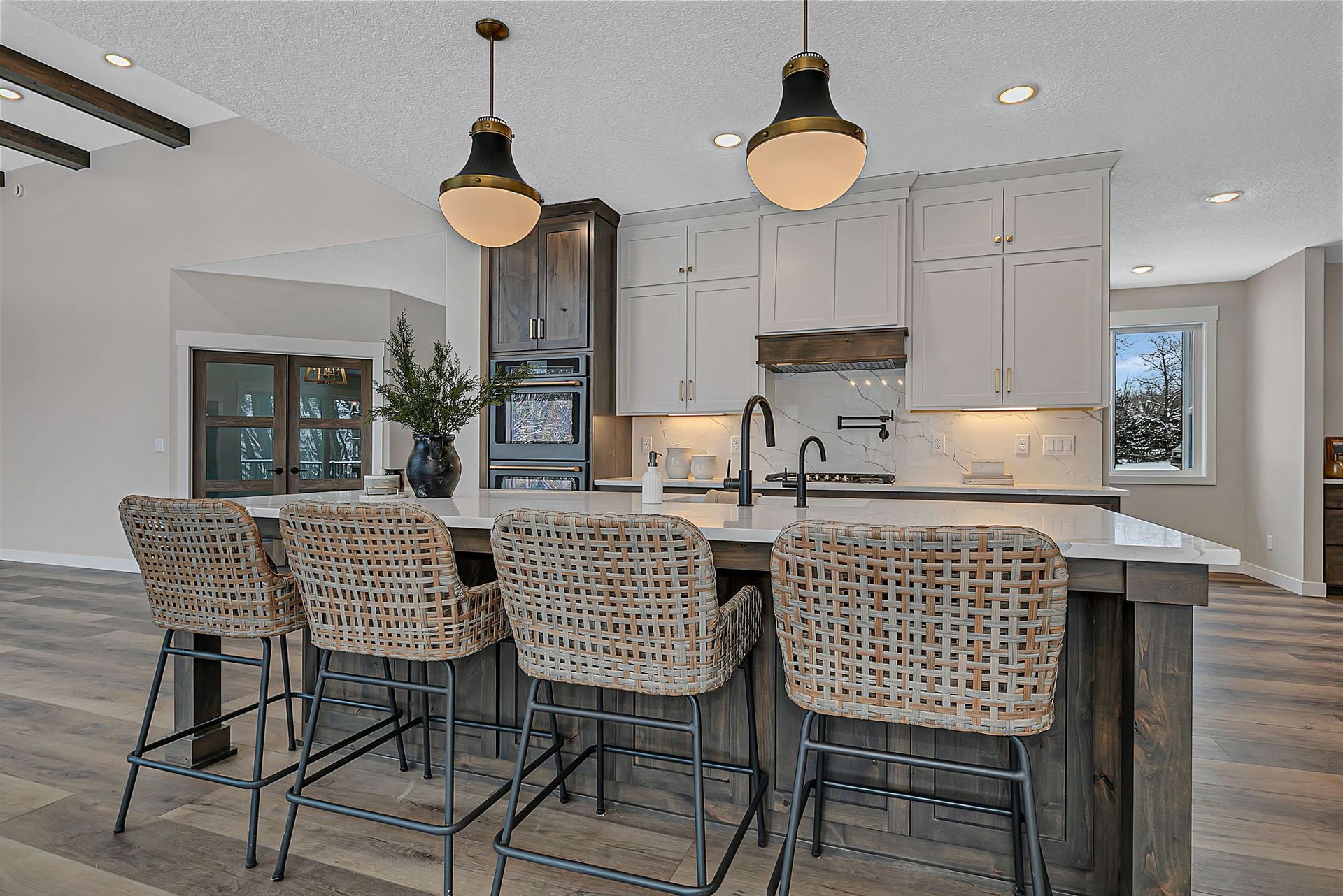 Kitchen island with woven bar stools, pendant lights, and cabinetry.