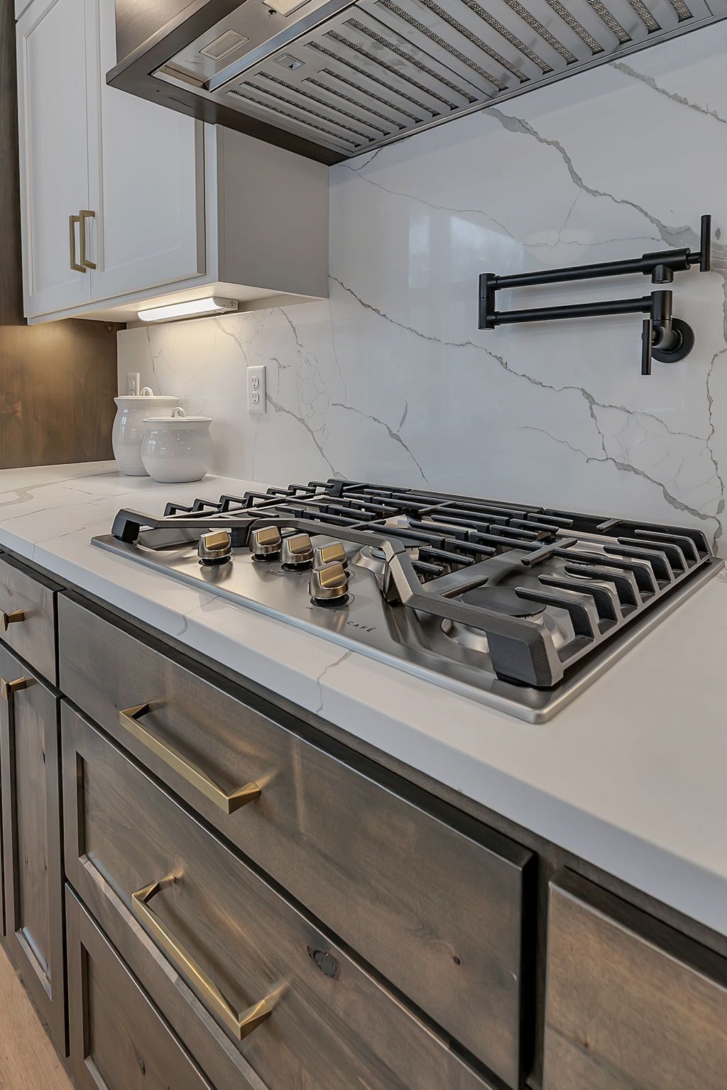 Modern kitchen with stovetop, marble backsplash, and two-tone cabinets.