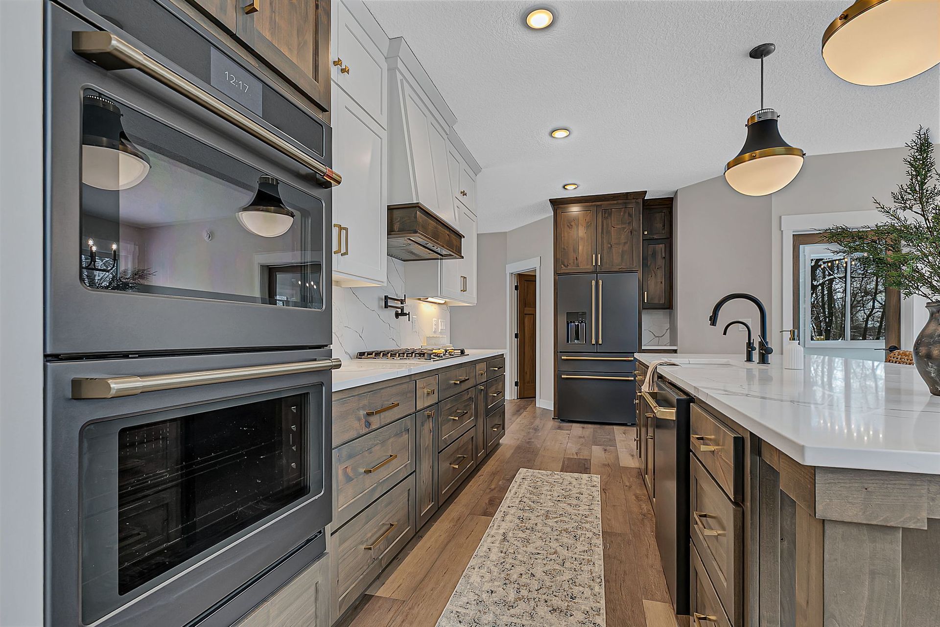 Modern kitchen with gray and light wood cabinets, double ovens, and island with a sink.