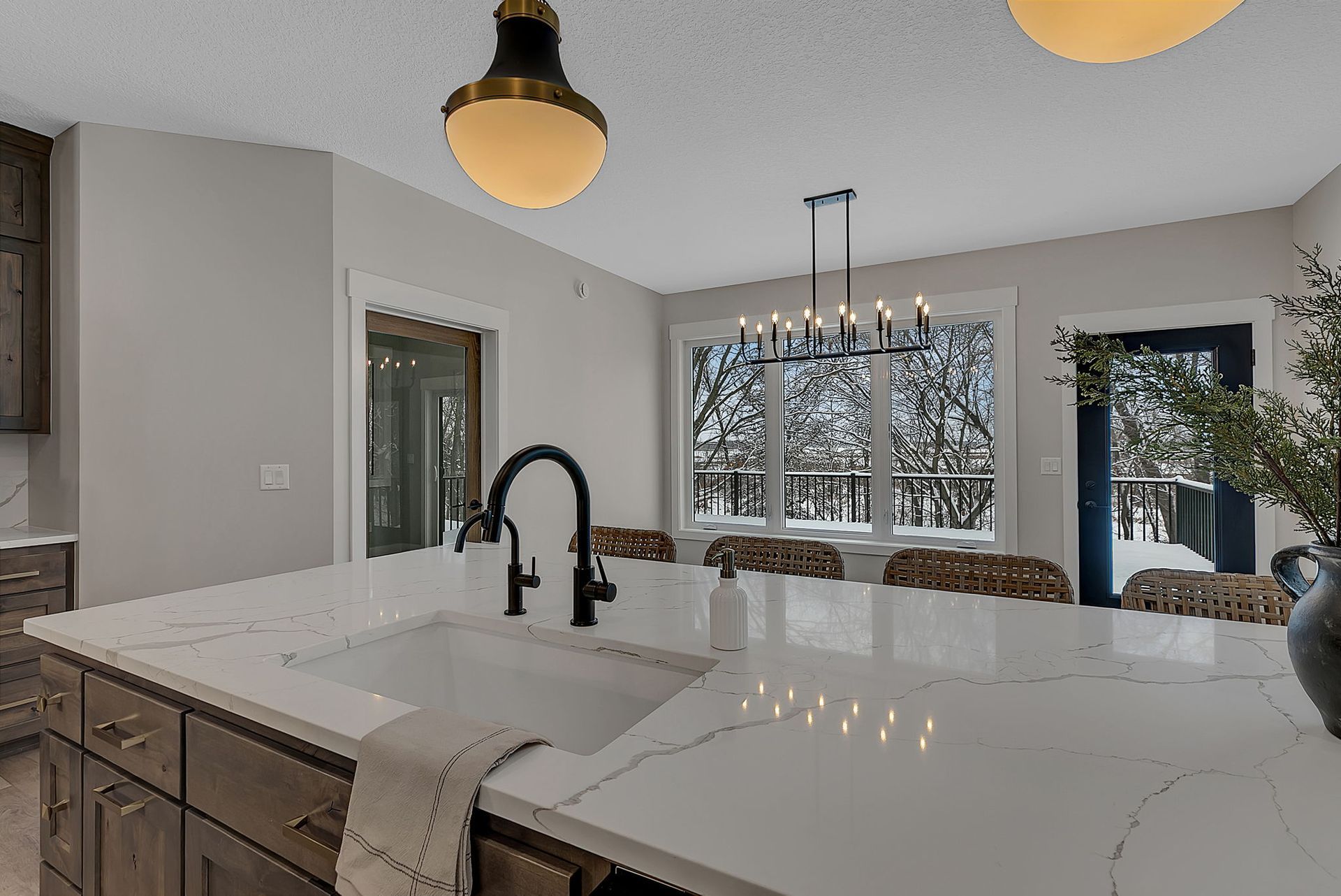Kitchen with white countertop, black faucet, and chandelier over a table near a window overlooking a snowy landscape.