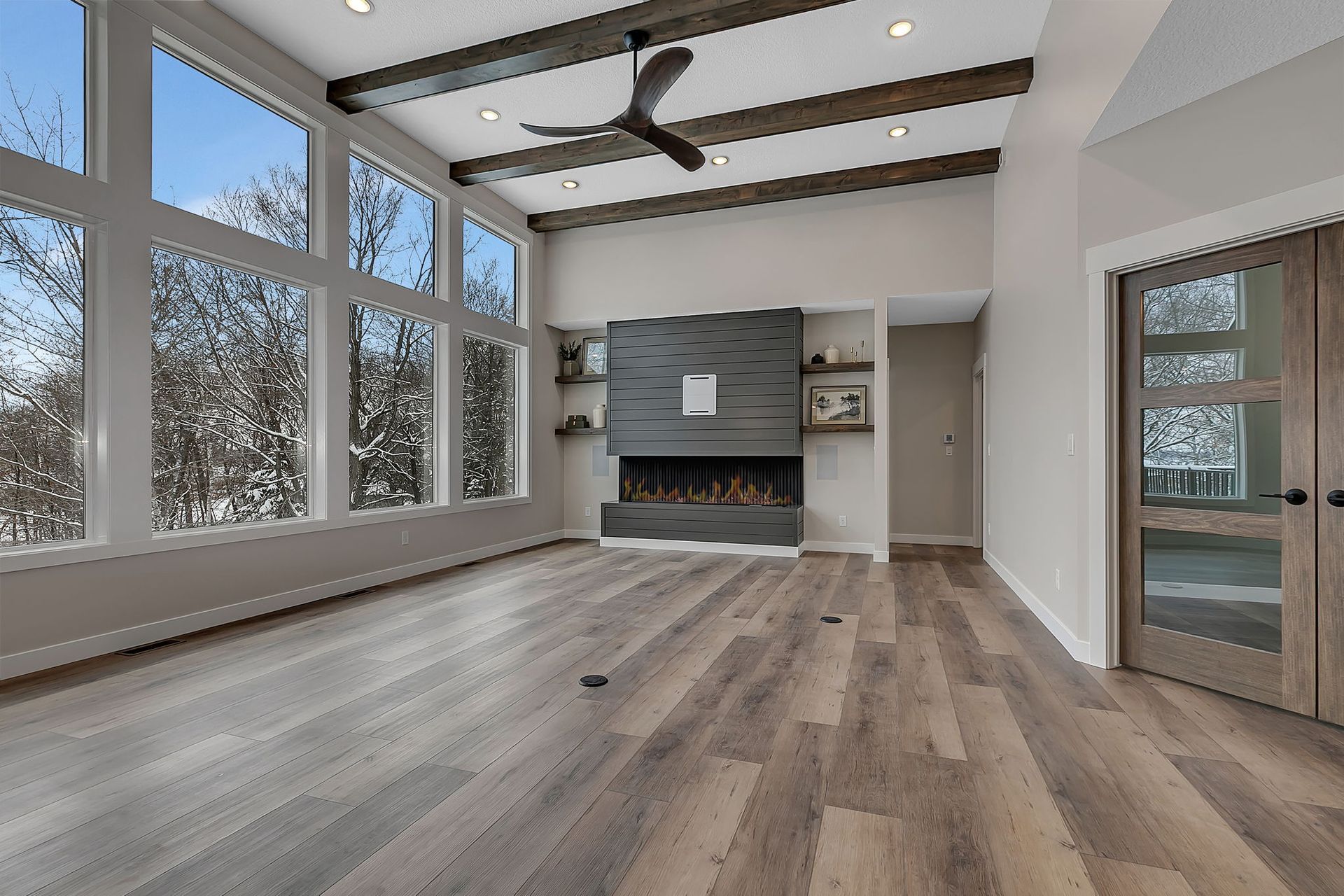 Living room with large windows, fireplace, wooden beams, and wood flooring.