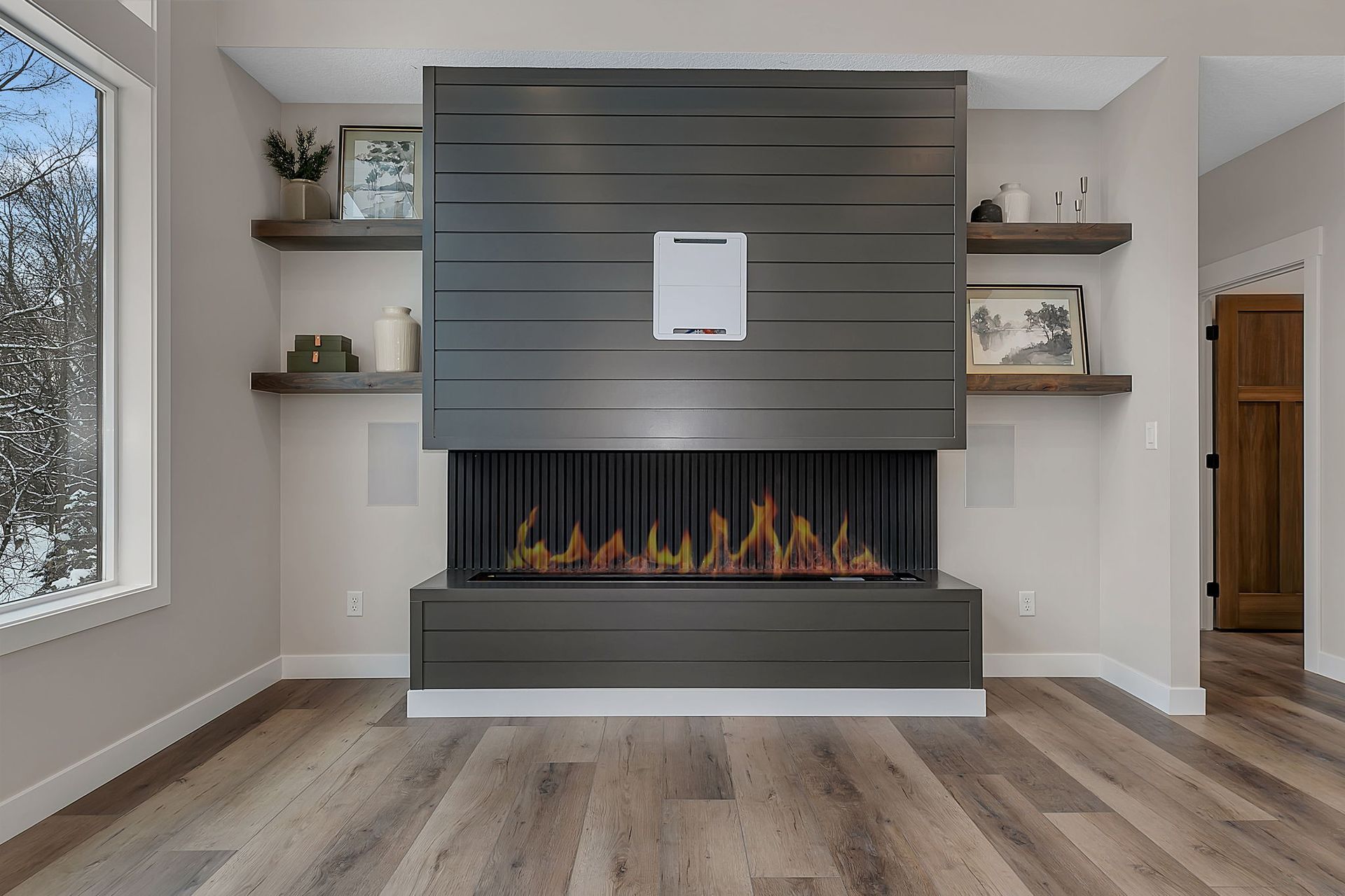 Modern living room with fireplace, gray paneling, floating shelves, and hardwood floors.