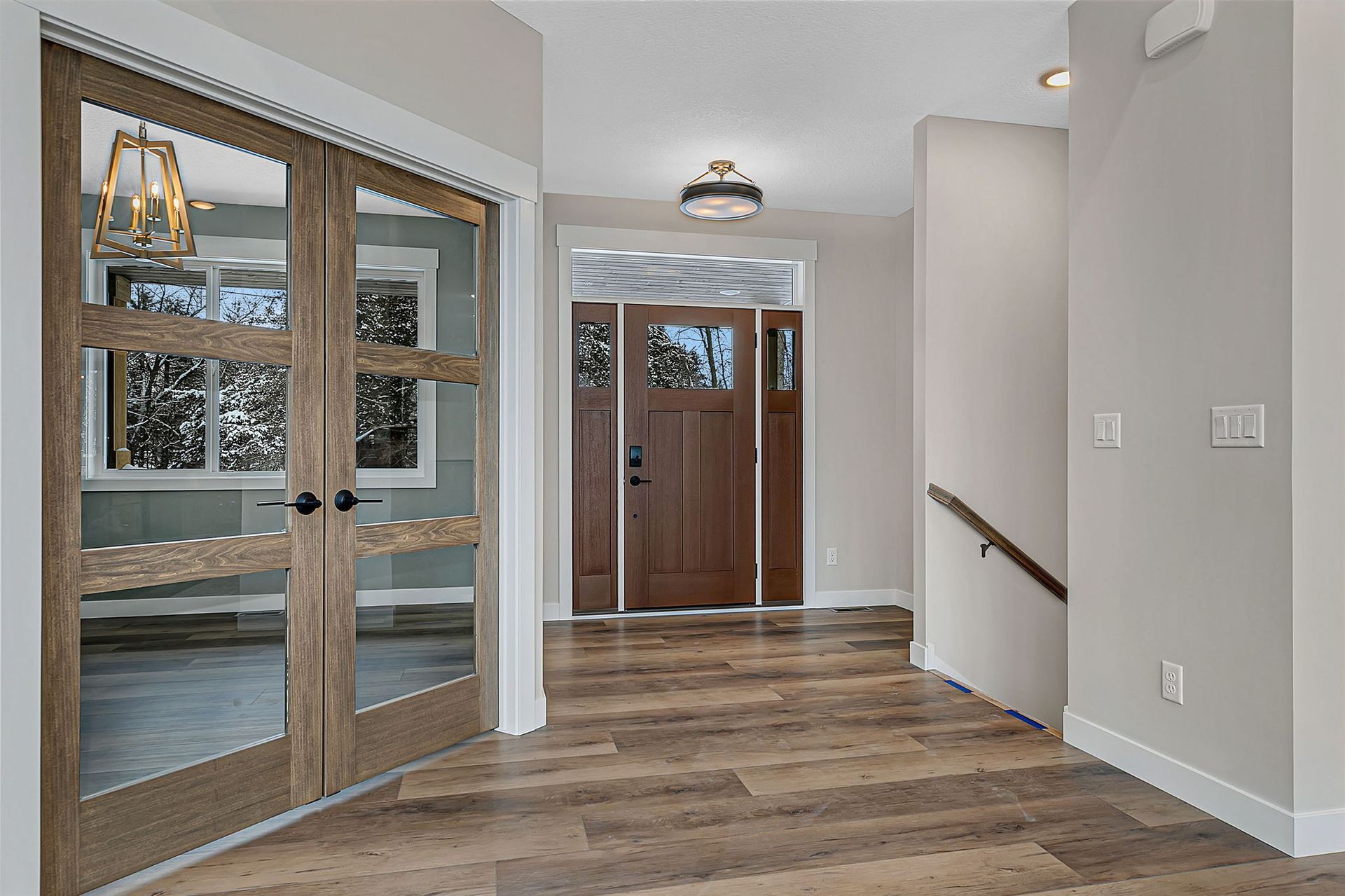 Entryway with wooden doors, a front door, and a staircase, all with neutral colored walls and flooring.