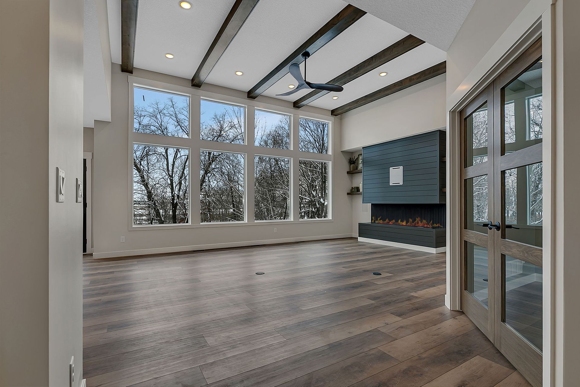 Modern living room with large windows, fireplace, and wood flooring.