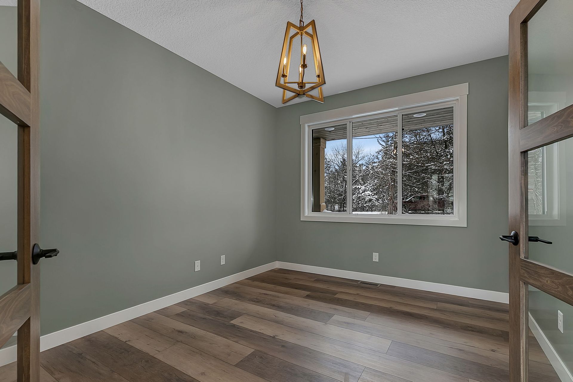 Empty room with gray walls, wood floors, and a window overlooking snowy trees.