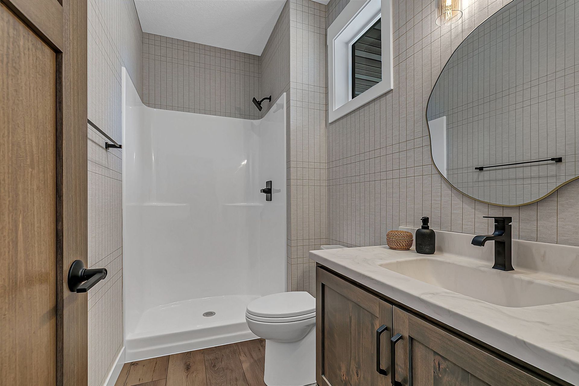 Bathroom with white shower, toilet, wooden vanity, and large round mirror.