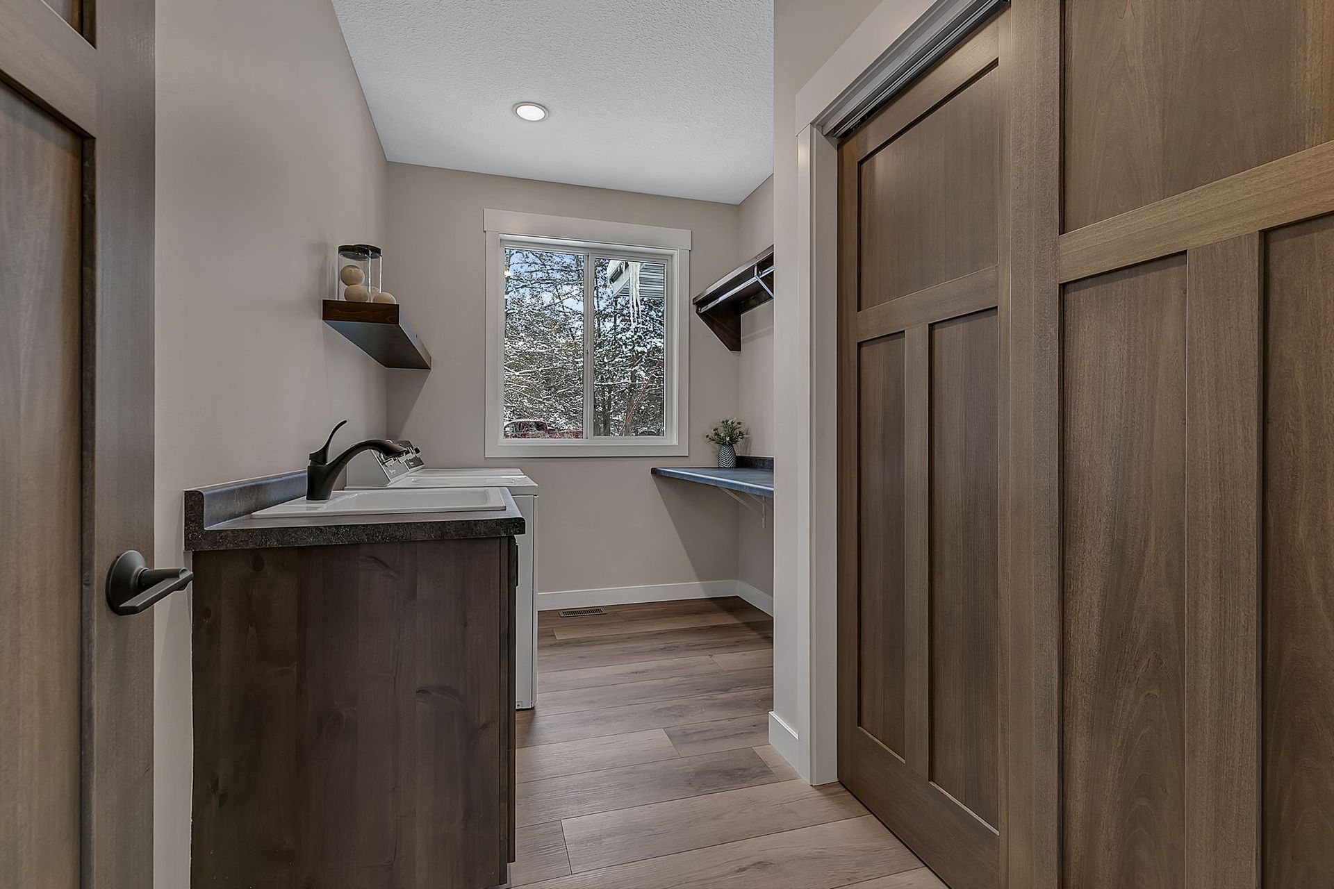 Laundry room with wooden cabinets, countertop, and window, with sliding closet doors on the right.