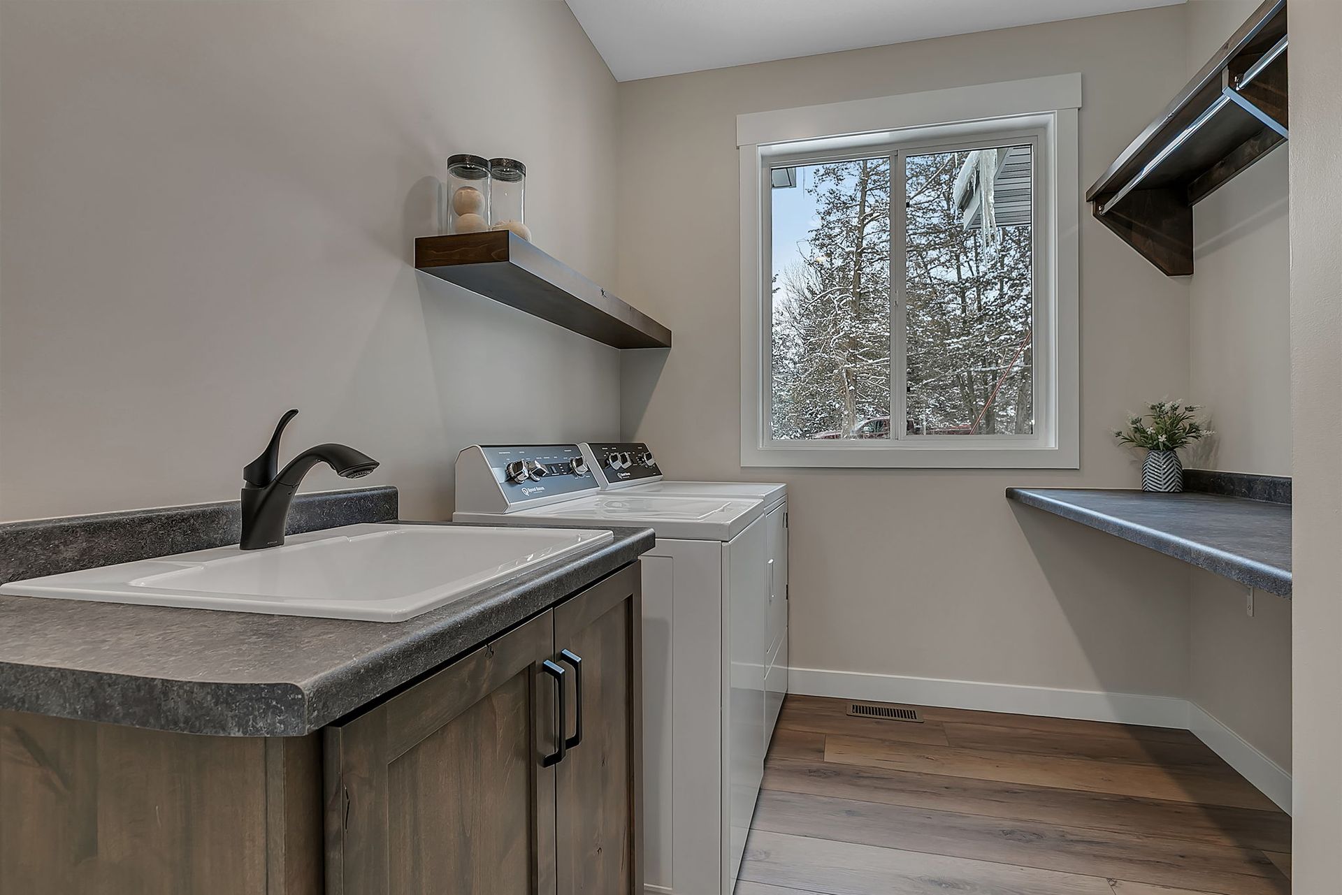 Laundry room with a washer, sink, shelves, and a window overlooking a snowy landscape.