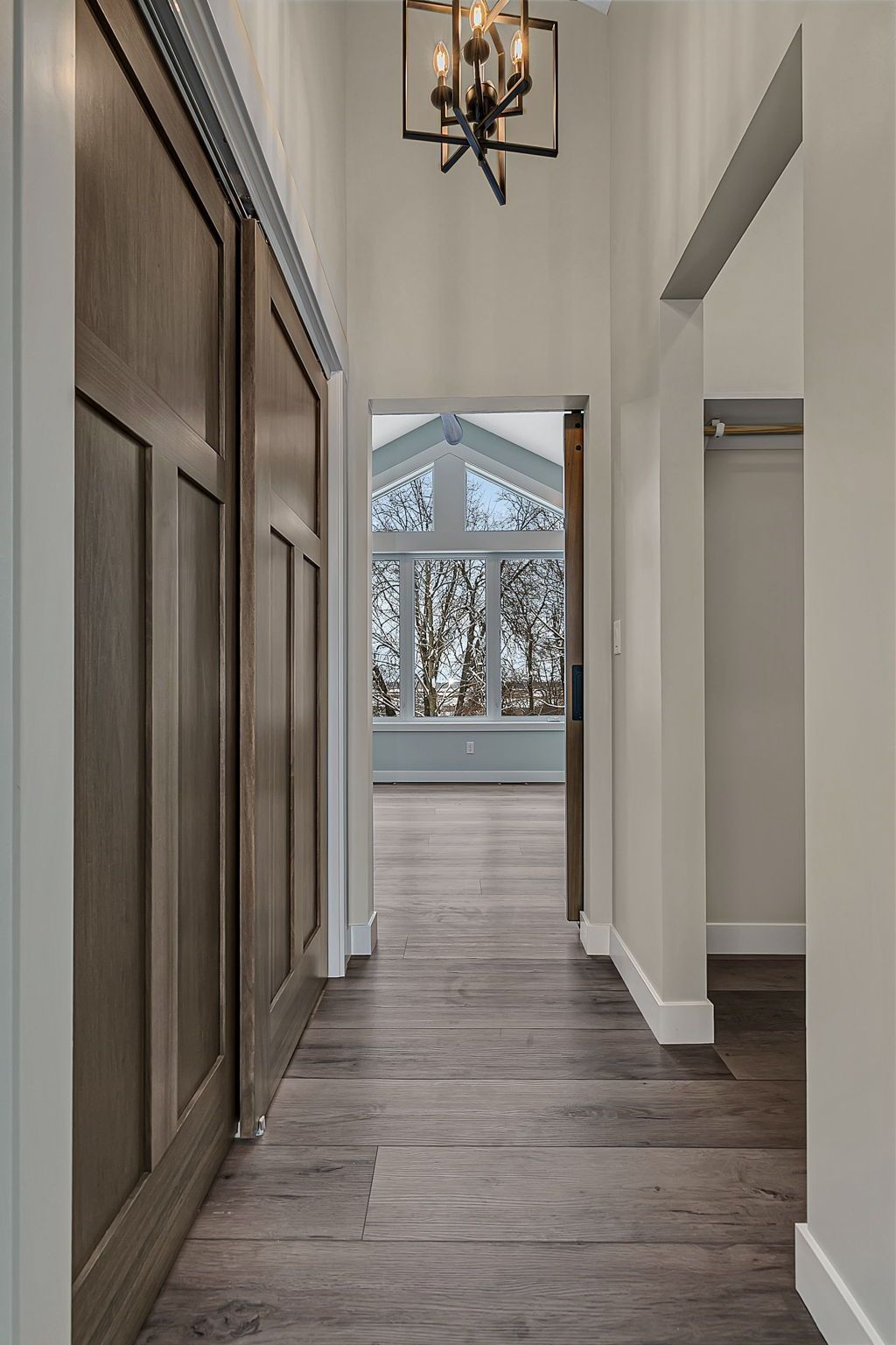 Hallway with wood floors, closet doors on the left, and a bright room with a large window at the end.