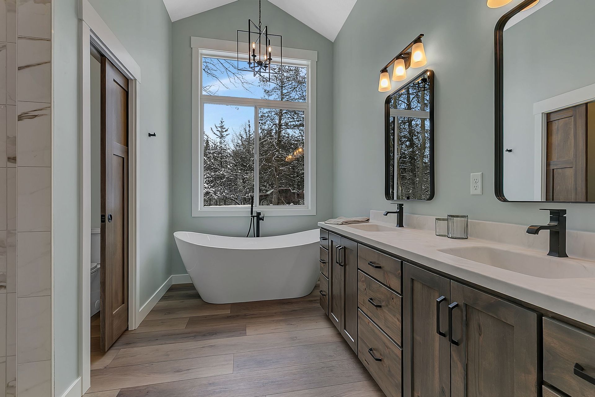 Bathroom with freestanding tub, double vanity, large window, and light blue walls.