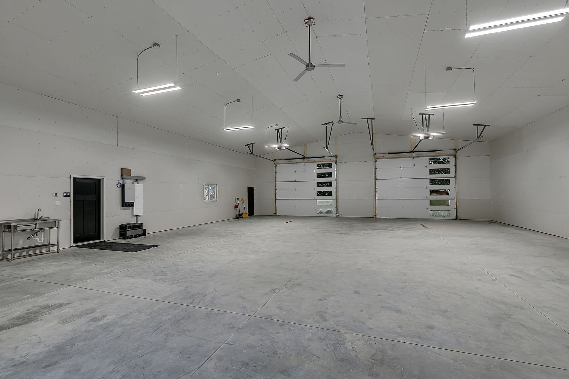 Empty, bright industrial space with concrete floor, overhead lighting, and garage doors in the back.