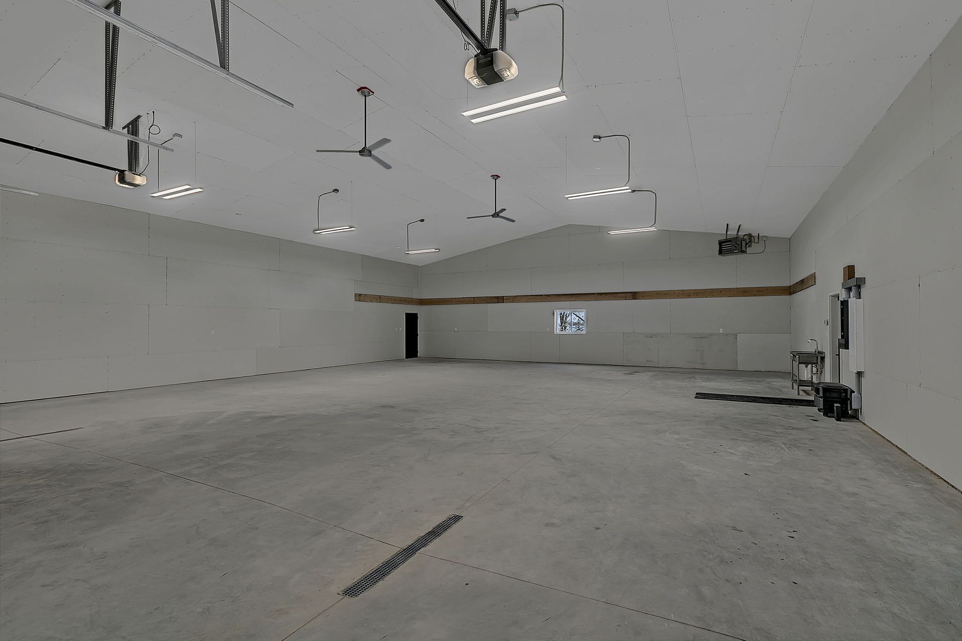 Empty warehouse interior with high ceilings, concrete floor, overhead lights, and garage door.