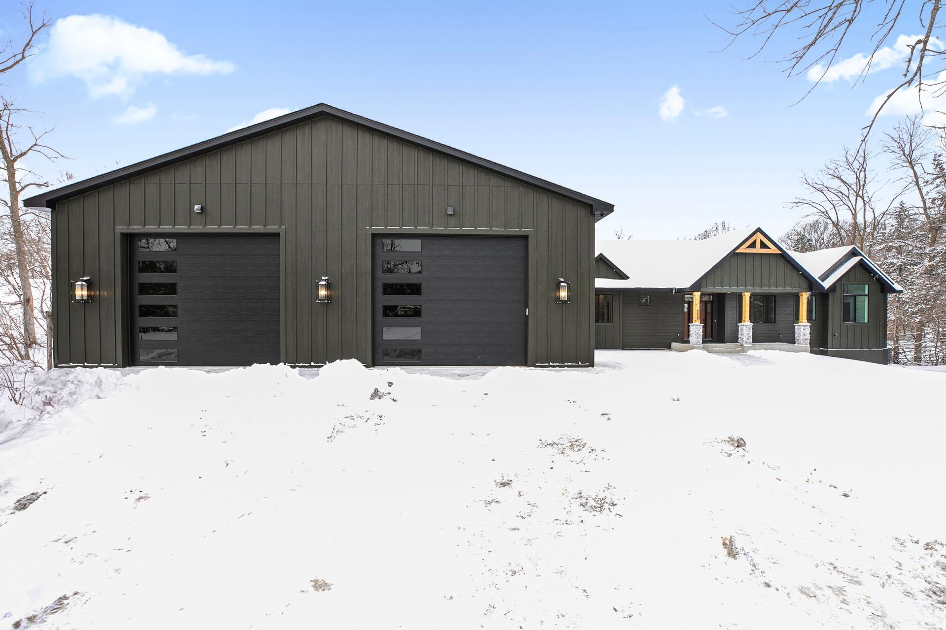 Black modern house and garage with snowy landscape.