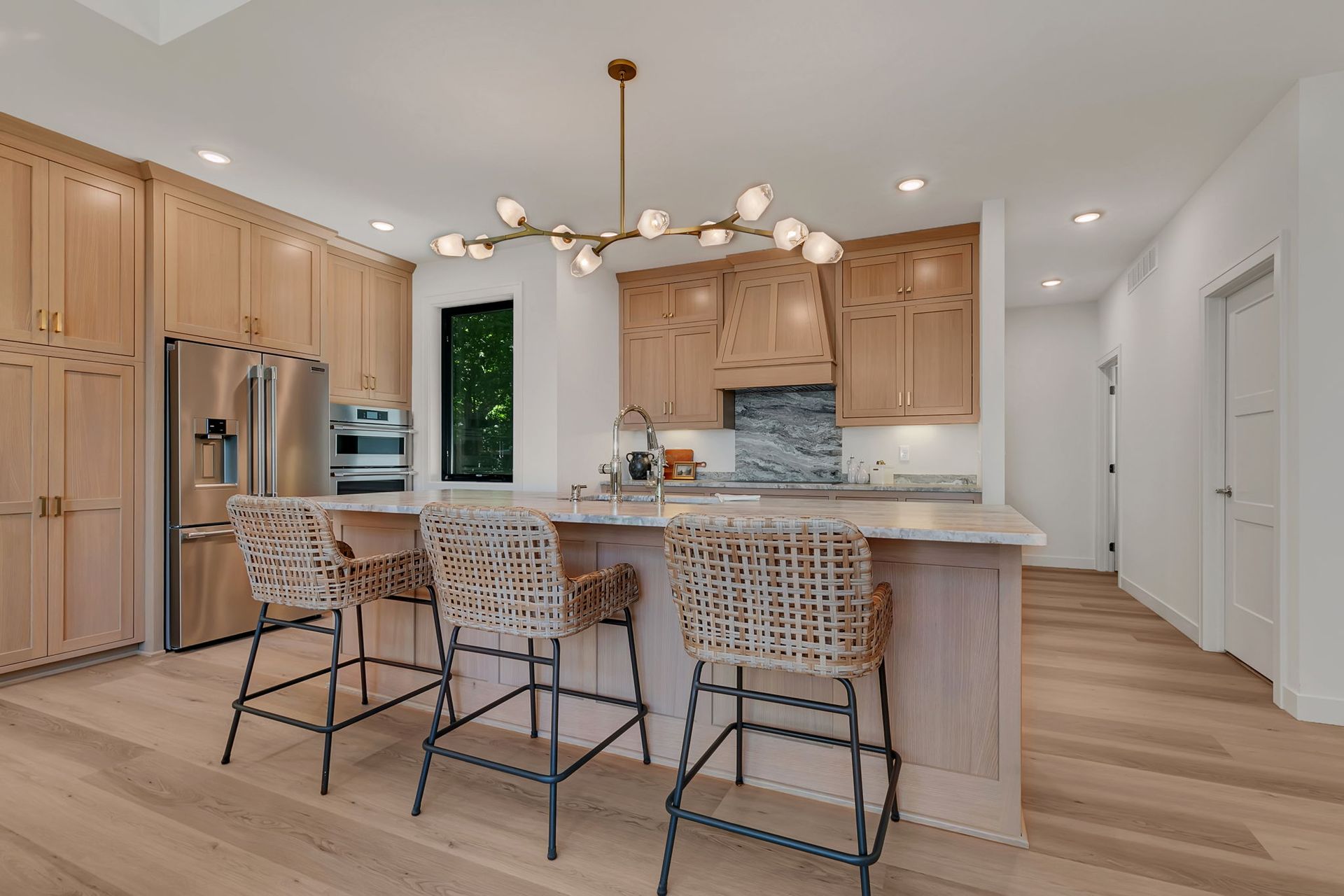 Bright modern kitchen with island, woven bar stools, wood cabinets, and a chandelier