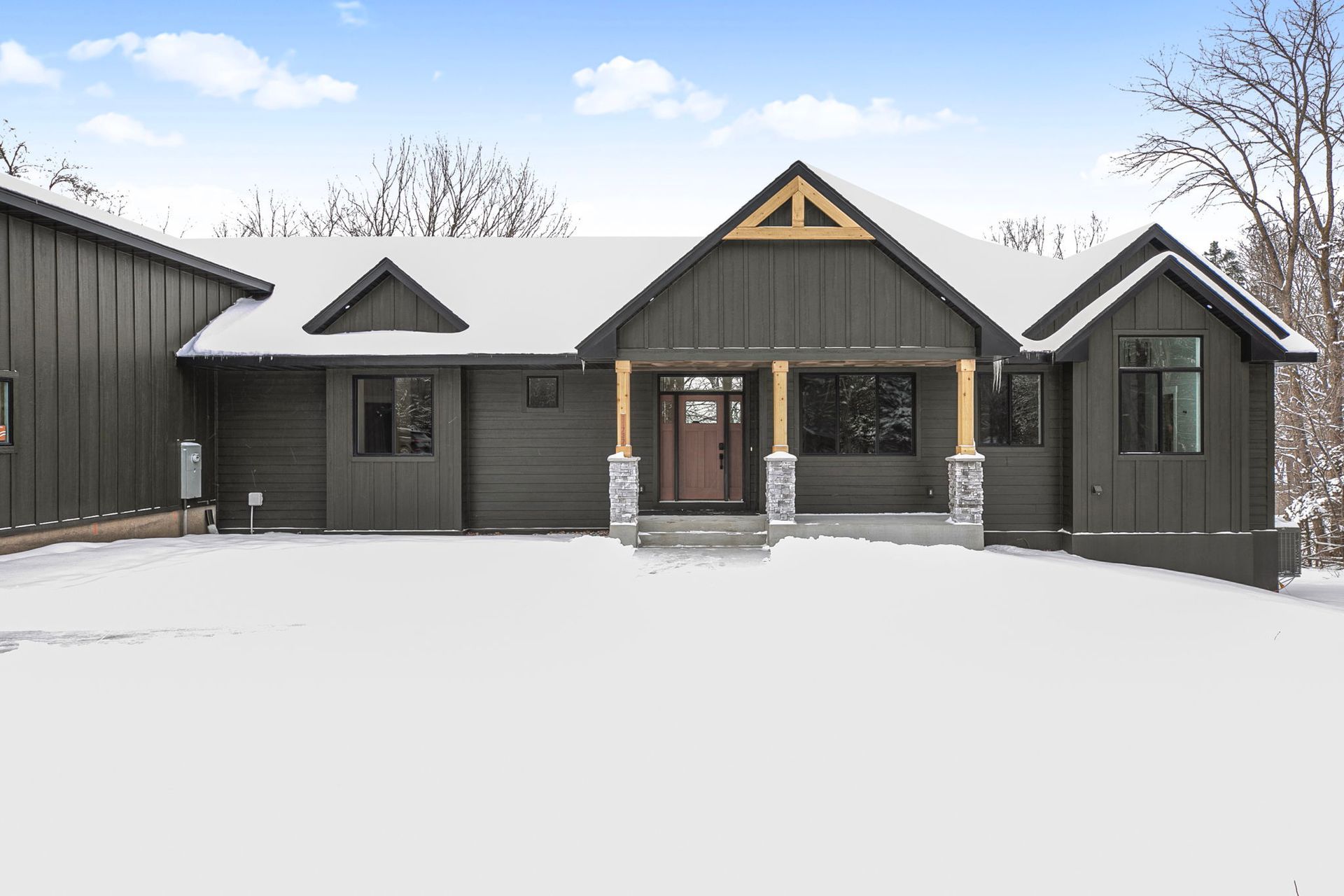 Dark gray house with a snow-covered yard, wooden porch, and a triangular roof design.
