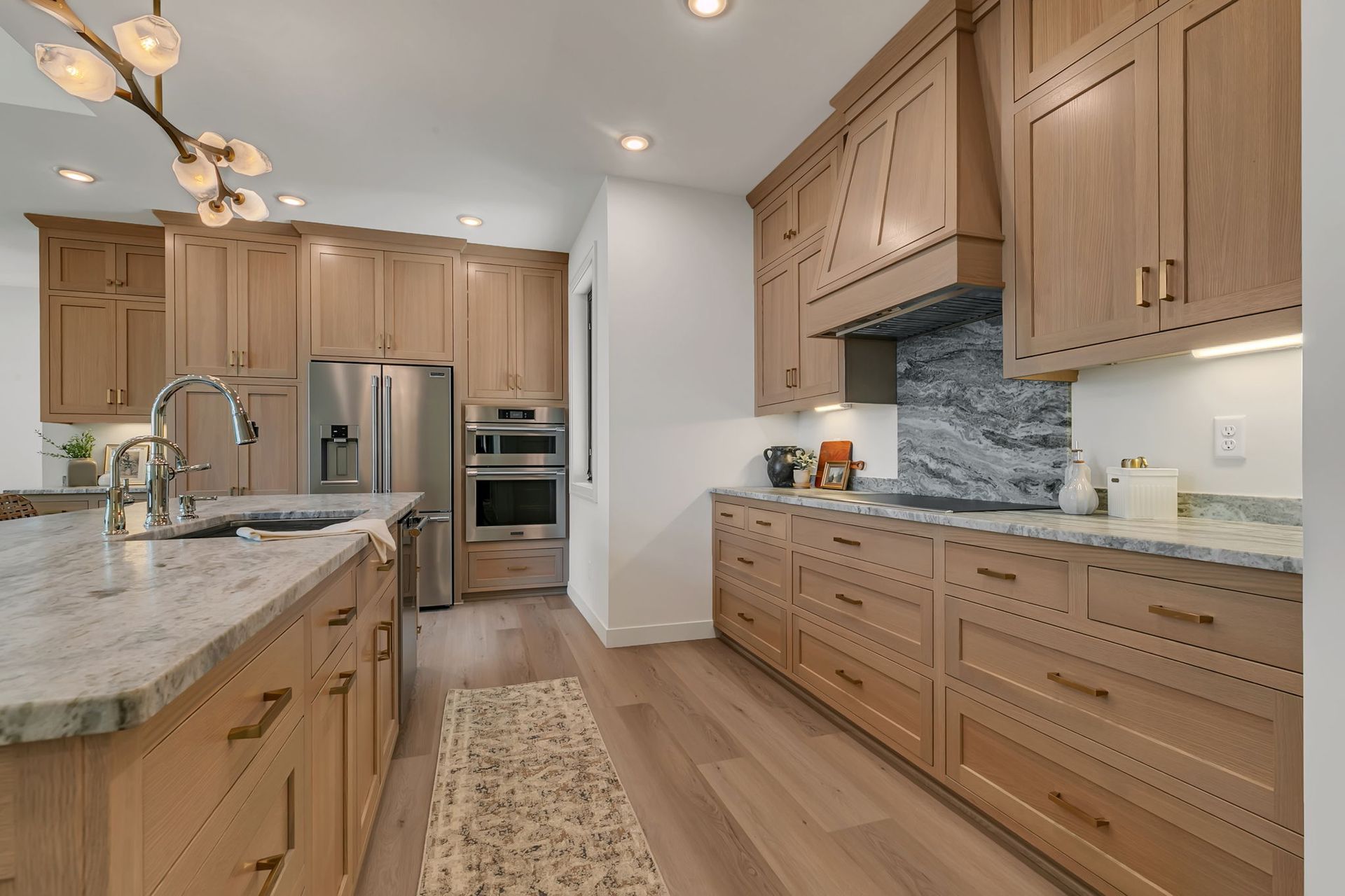Bright modern kitchen with wood cabinets, marble island, stainless steel appliances, and woven runner rug