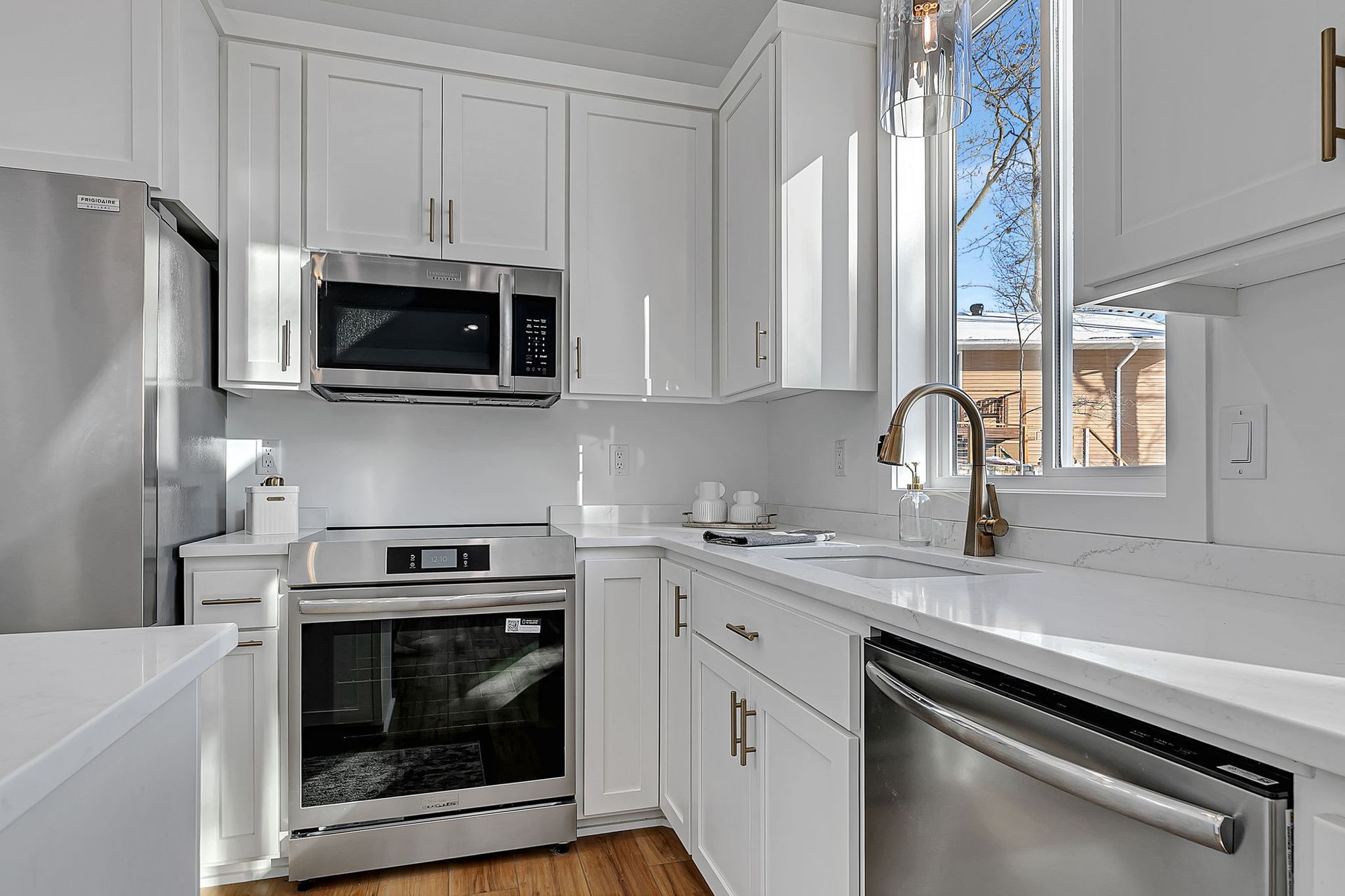 White kitchen with stainless steel appliances, white cabinets, and a window over the sink.