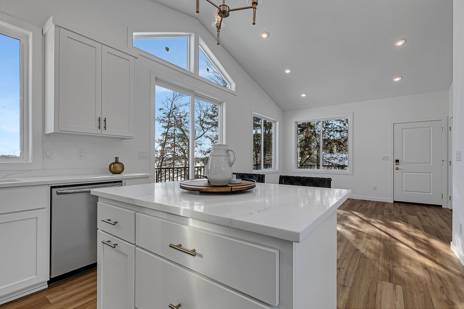 Bright, modern kitchen with white cabinets, island, and large windows overlooking trees.