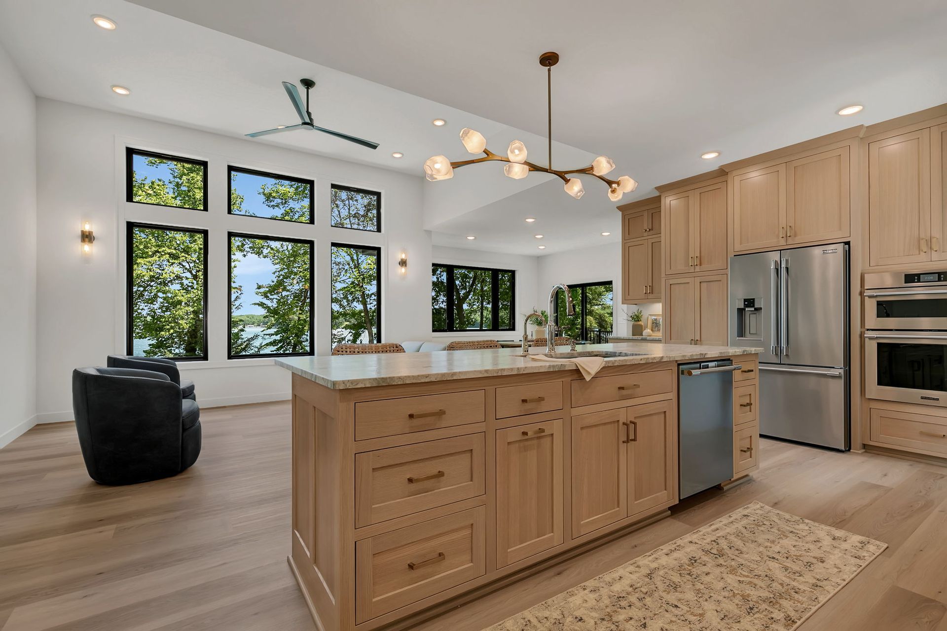 Bright modern kitchen with wood cabinets, island, stainless appliances, and large windows overlooking trees