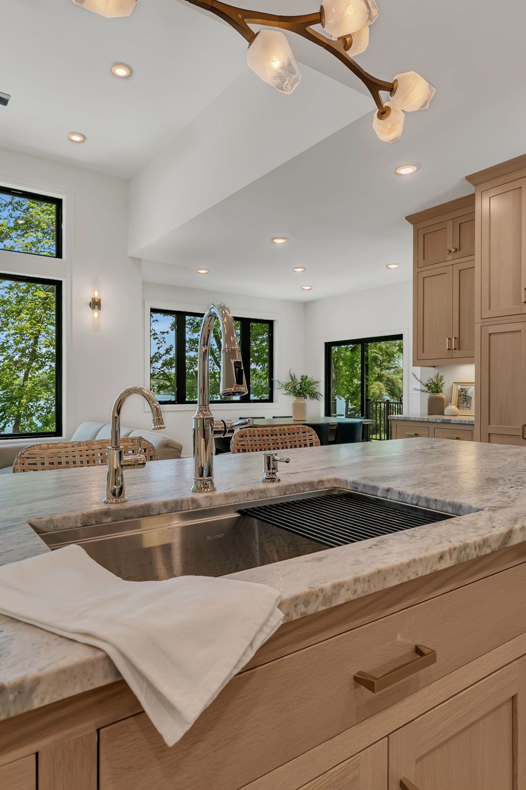 Bright kitchen with wood cabinets, marble island, sink, and large windows overlooking greenery