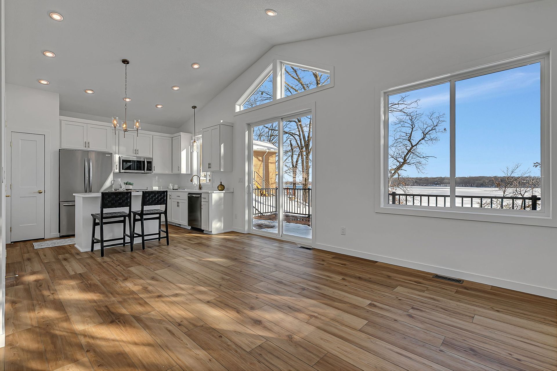 Bright open-concept living space with wood floors, white walls, and a view of a body of water through windows.