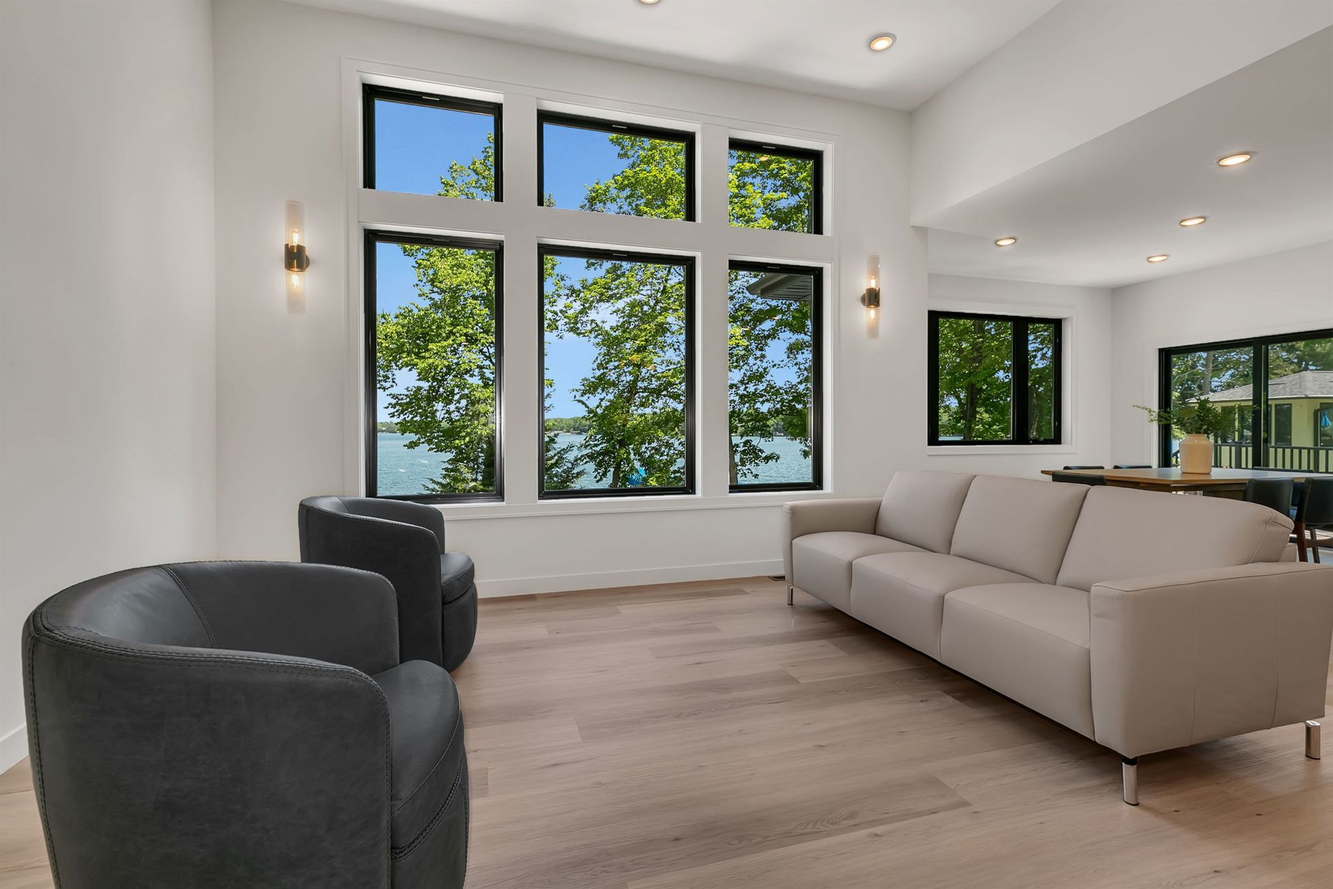Modern living room with large windows, beige sofa, and black chairs on light wood flooring