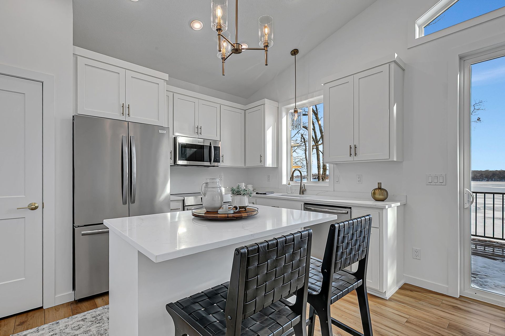 White kitchen with stainless steel appliances, island, and two black bar stools.