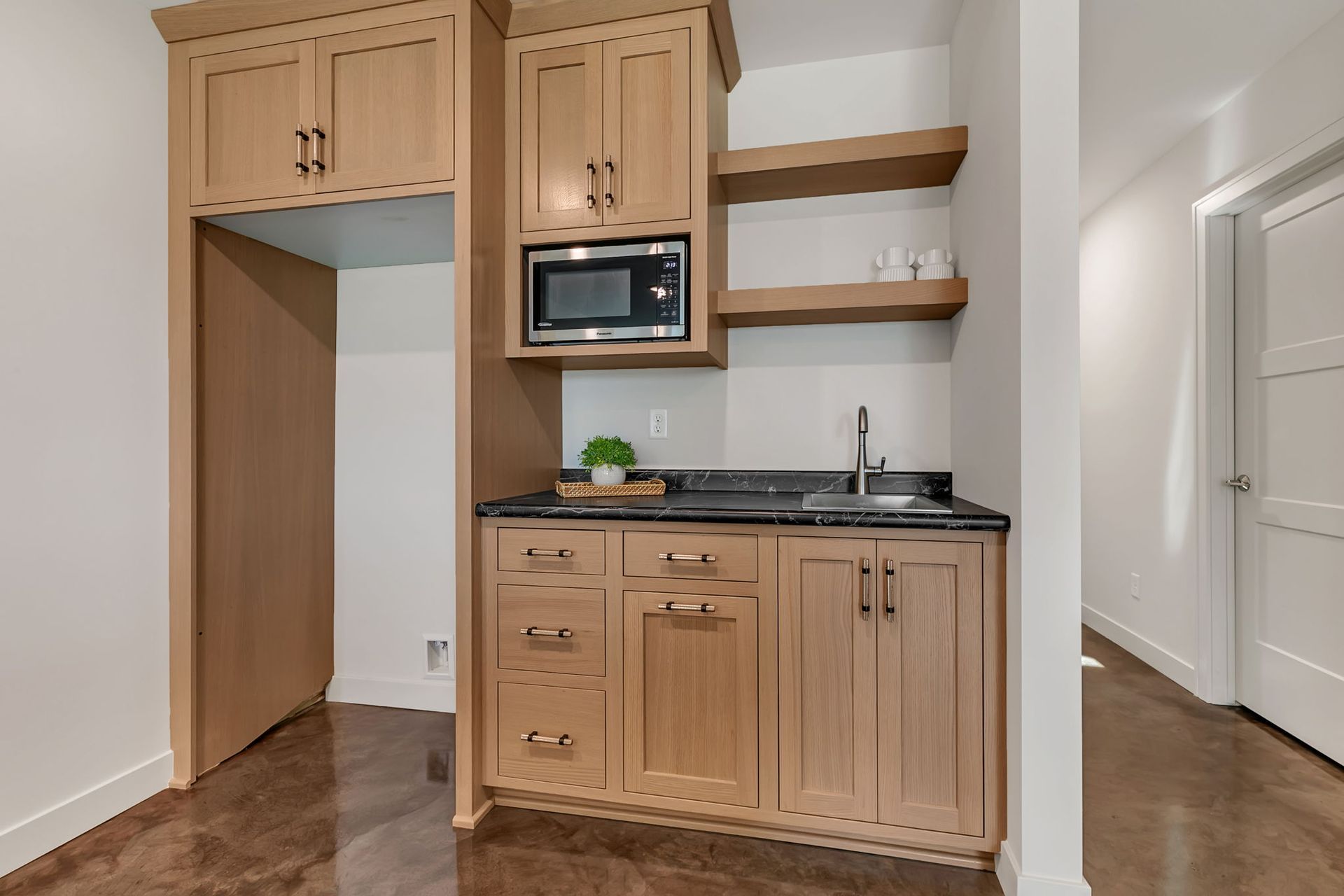 Compact wood kitchenette with microwave, sink, cabinets, and open shelves in a small room
