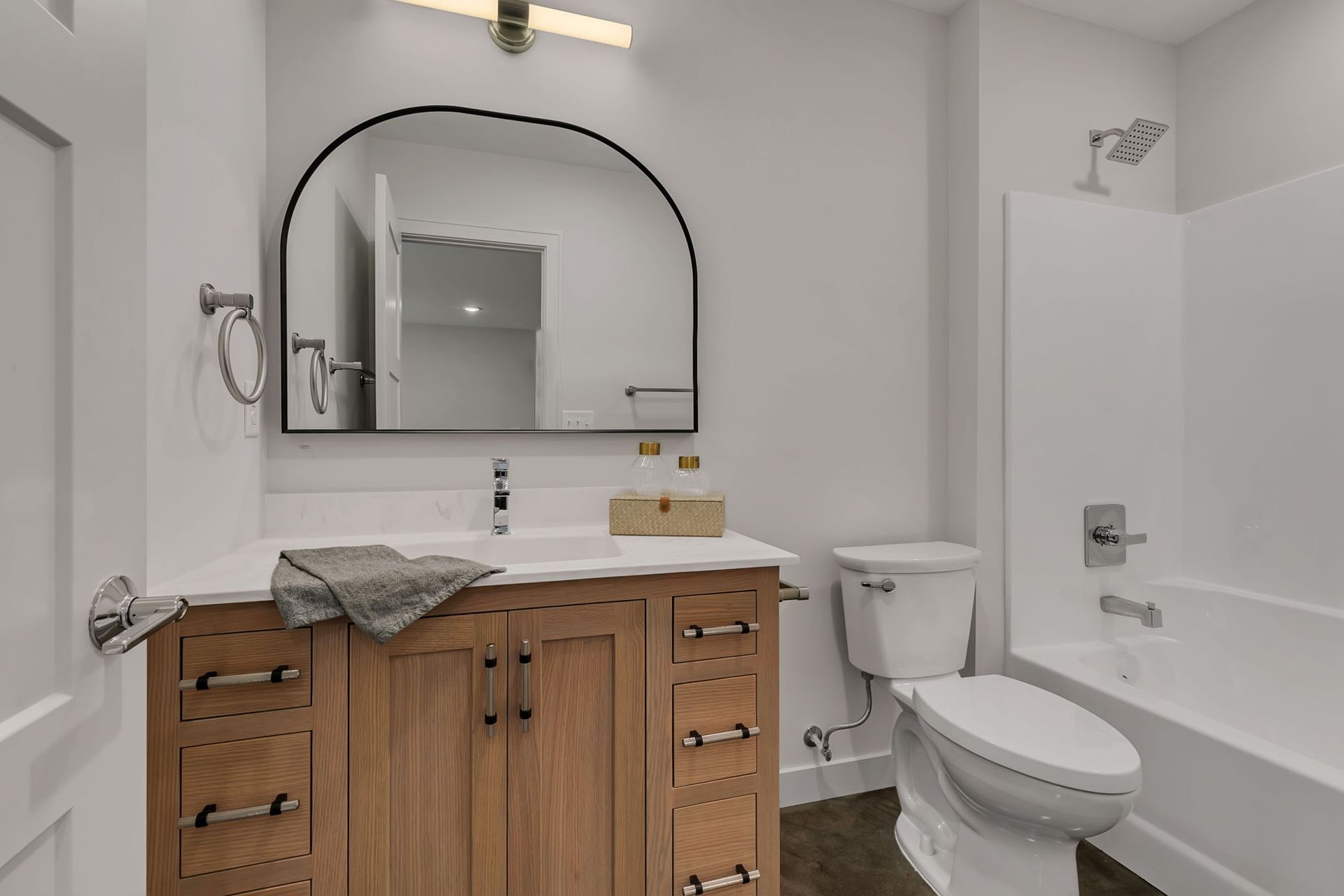 Modern bathroom with wood vanity, black-framed mirror, toilet, and bathtub.