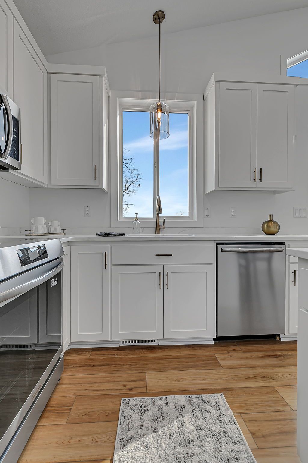 Bright white kitchen with a window above the sink and stainless steel appliances.