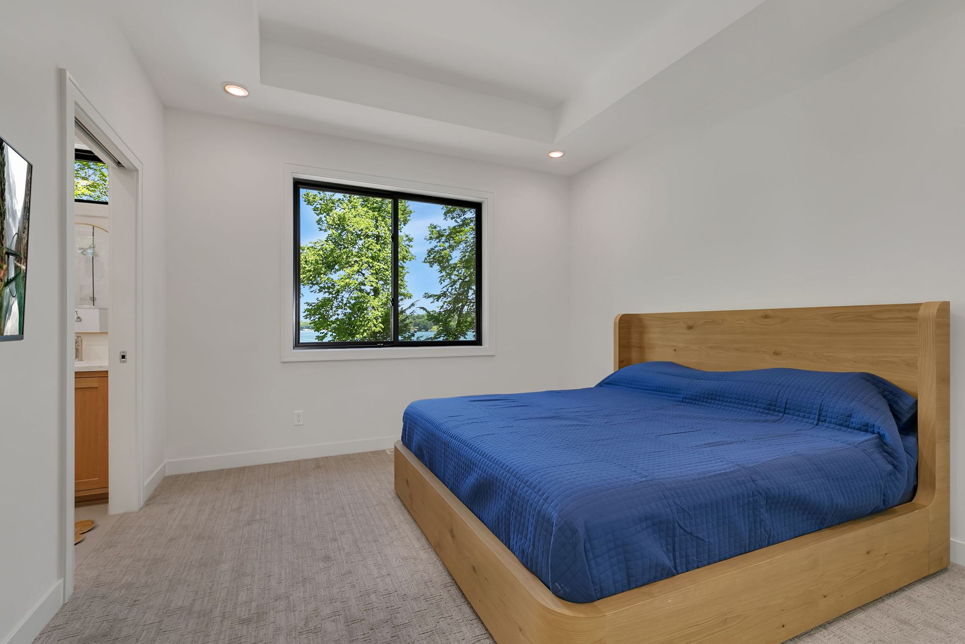 Minimal bedroom with blue bedspread, wood bed frame, and window view of trees