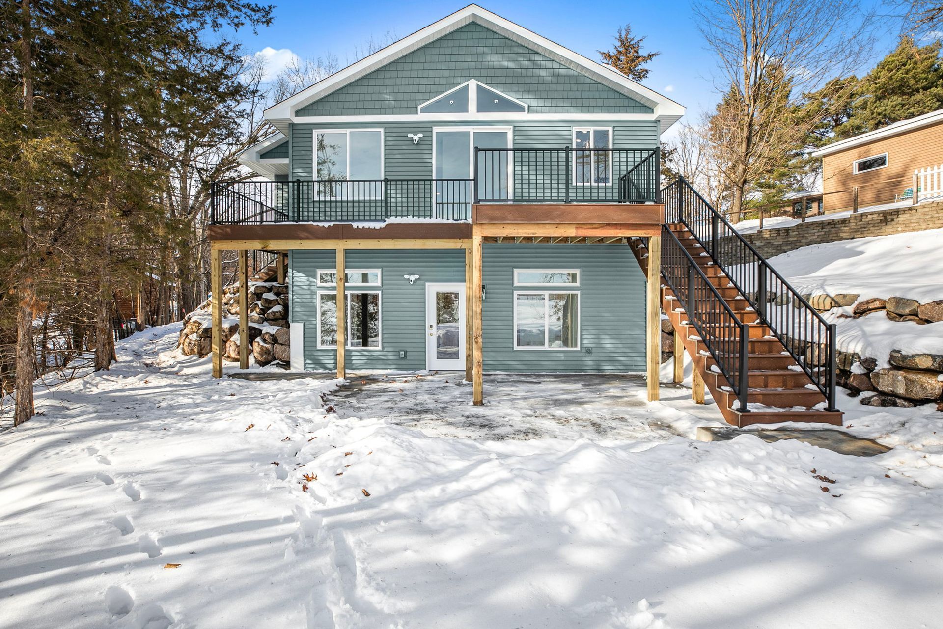 Blue house with two-story deck, stairs, and snow-covered yard. Winter scene.