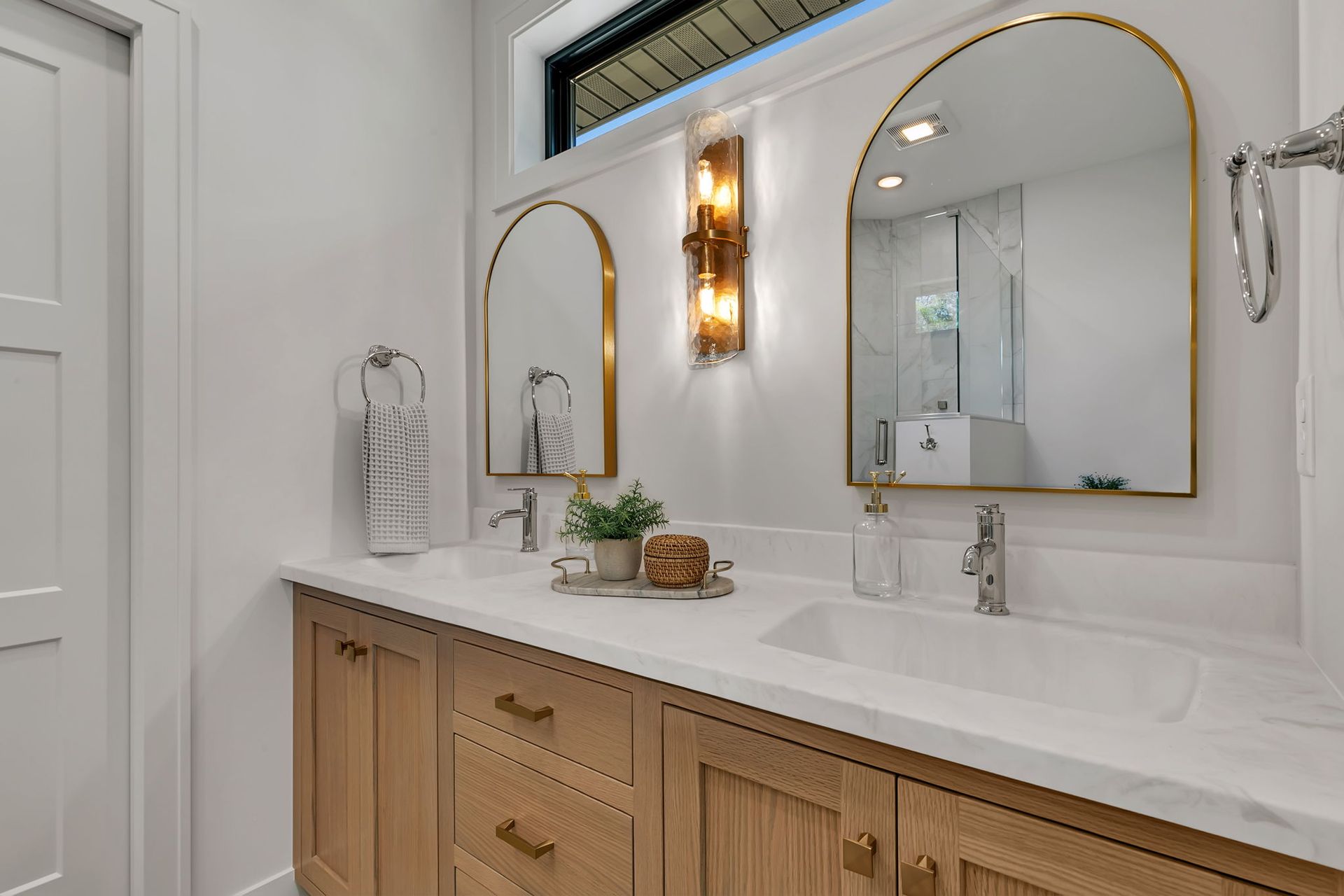 Bright bathroom vanity with double gold-framed mirrors, white countertop, wood cabinets, and wall sconce lights