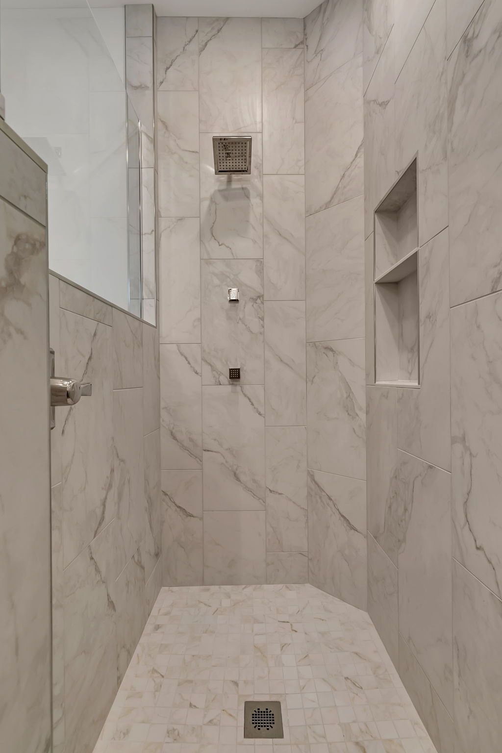 Marble-tiled shower with multiple wall niches and floor drain, viewed from the entrance