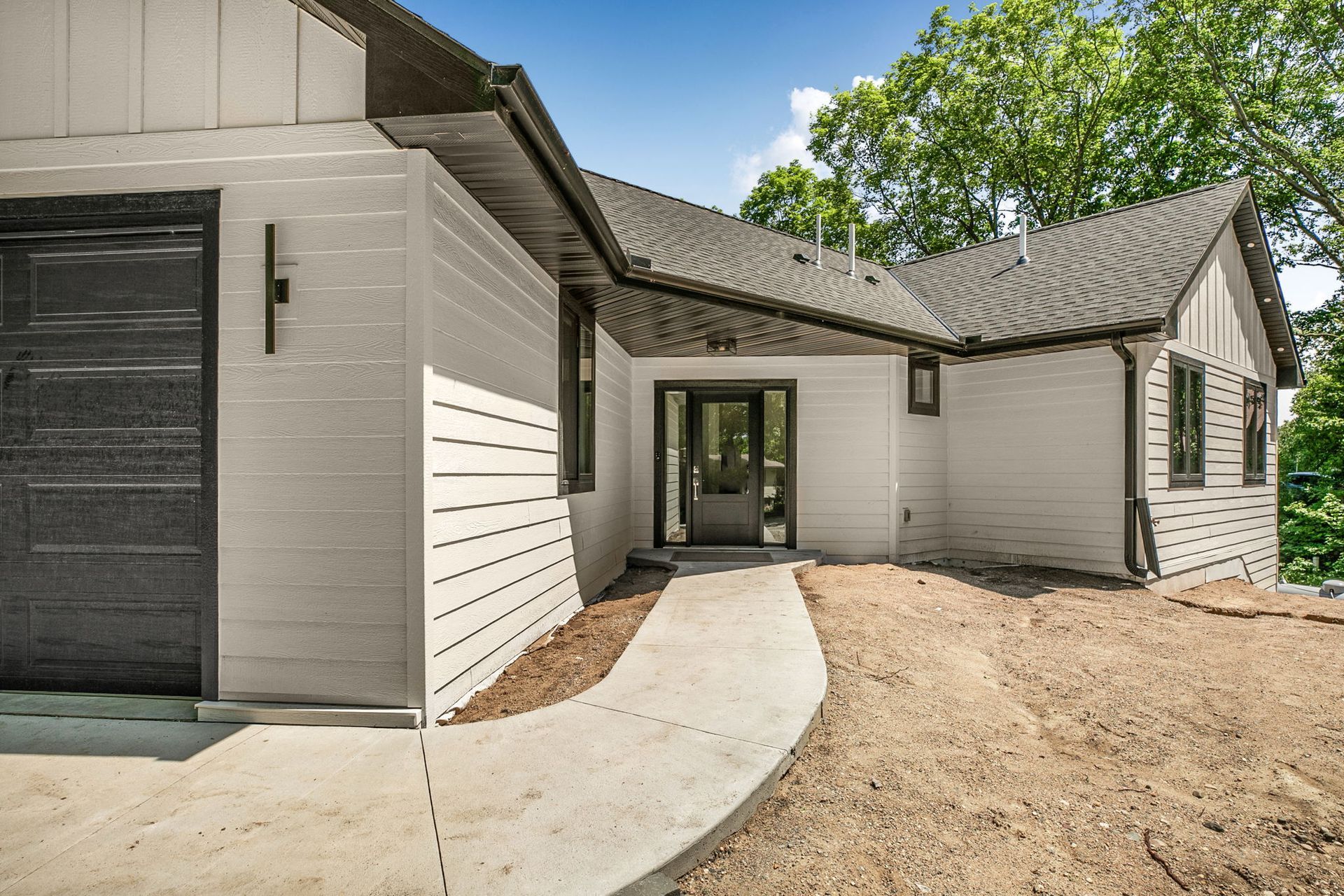 Modern white house exterior with curved concrete walkway and dirt landscaping