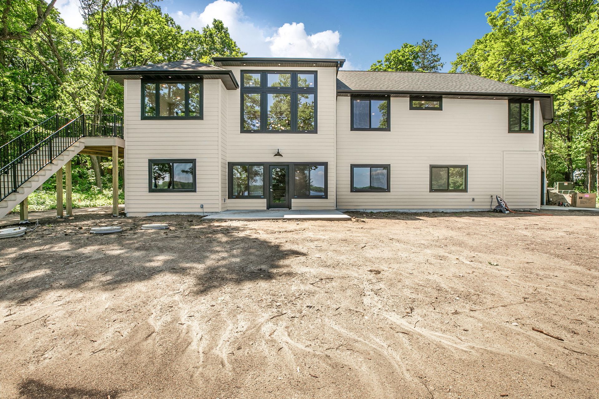Modern two-story beige house with large windows and a dirt front yard