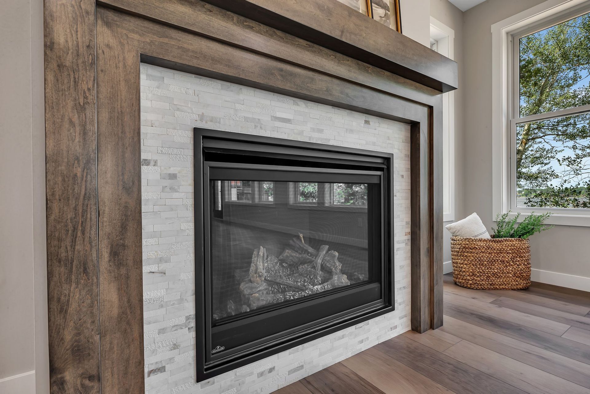 A fireplace with a wooden mantle in a living room next to a window.