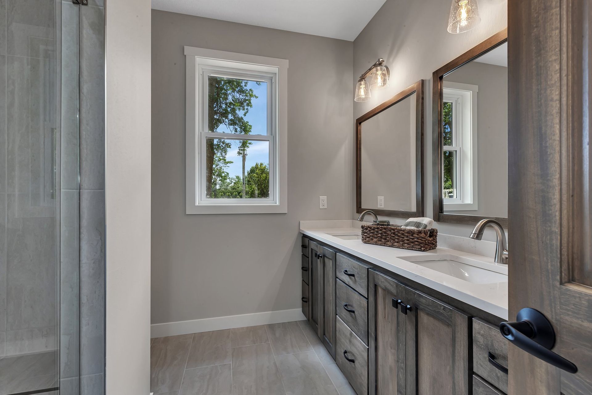 A bathroom with two sinks , two mirrors and a window.