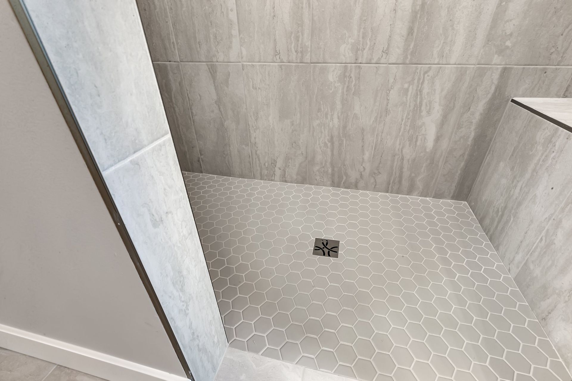 A walk in shower with a tiled floor and a drain.
