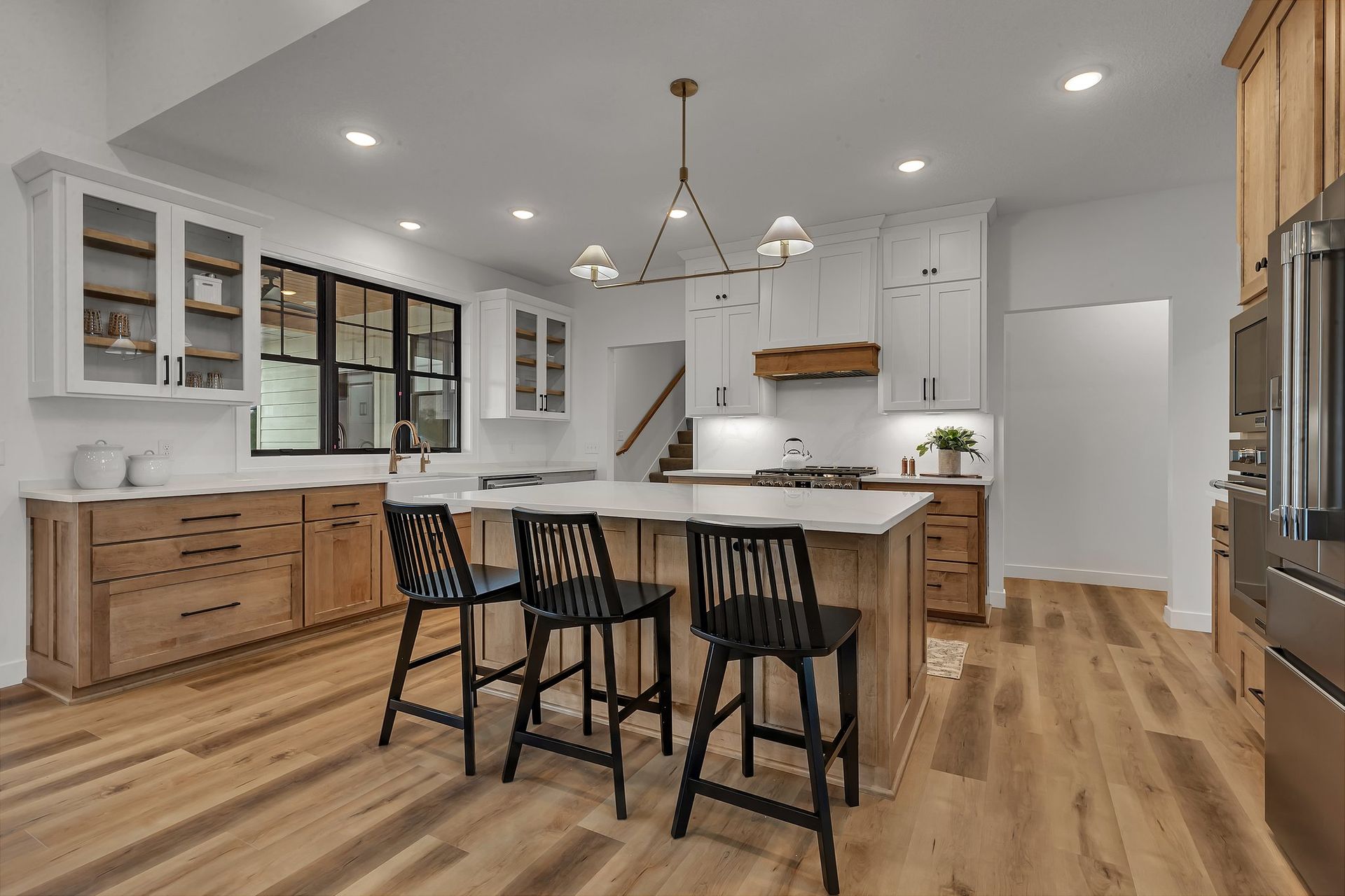 A kitchen with wooden floors , white cabinets , stainless steel appliances and a large island.