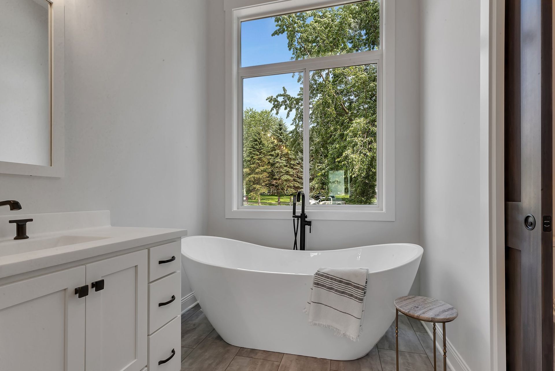 A bathroom with a tub , sink , mirror and window.