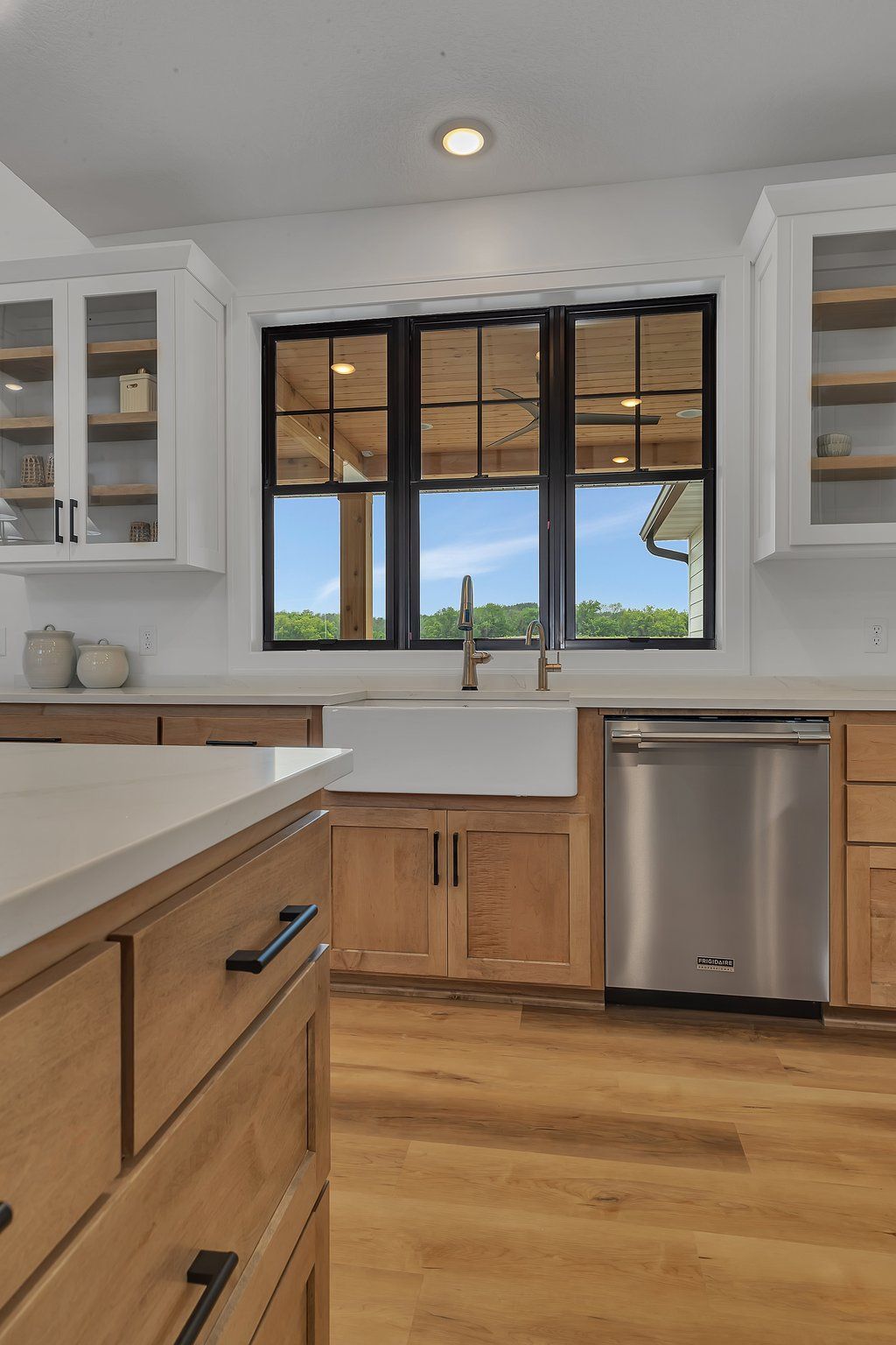 A kitchen with wooden cabinets , stainless steel appliances , a sink , and a large window.